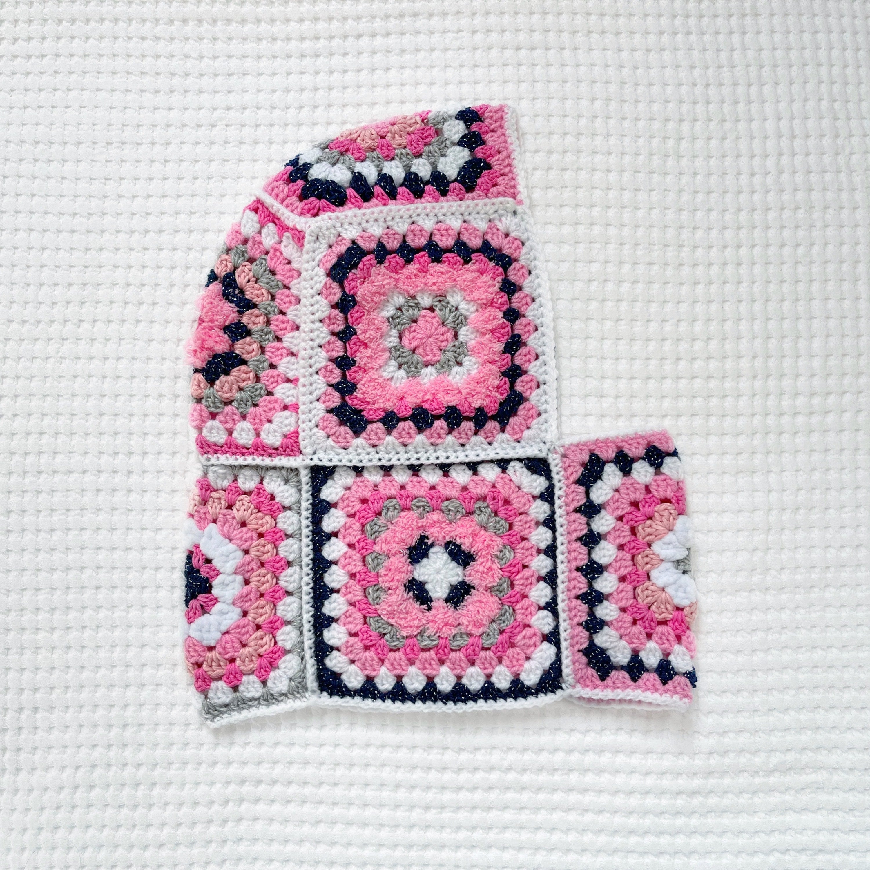 Crocheted balaclava with pink and blue square patterns on a white background