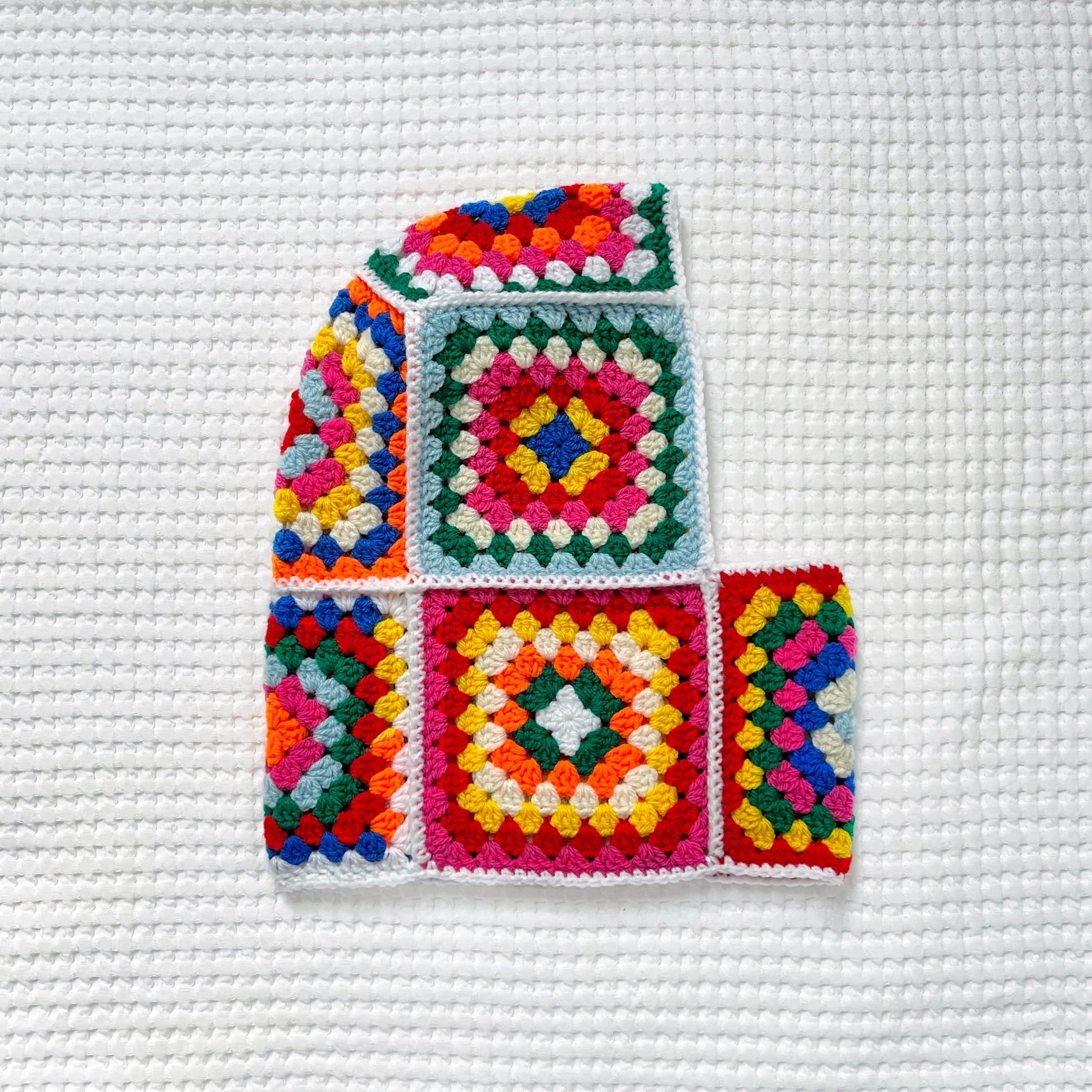 Colorful crocheted granny square balaclava on a white textured background