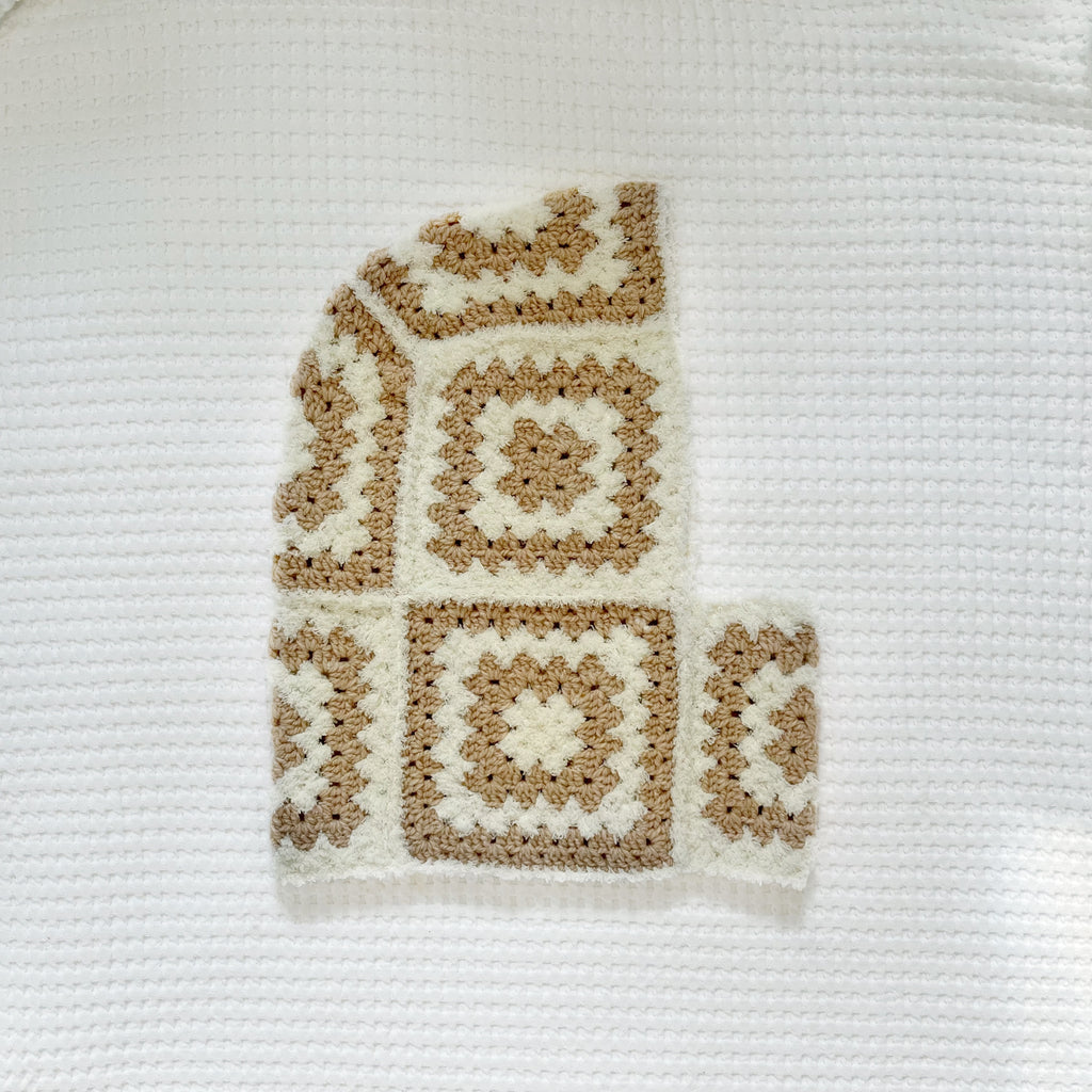 Crocheted balaclava in beige and white colors on a textured white background