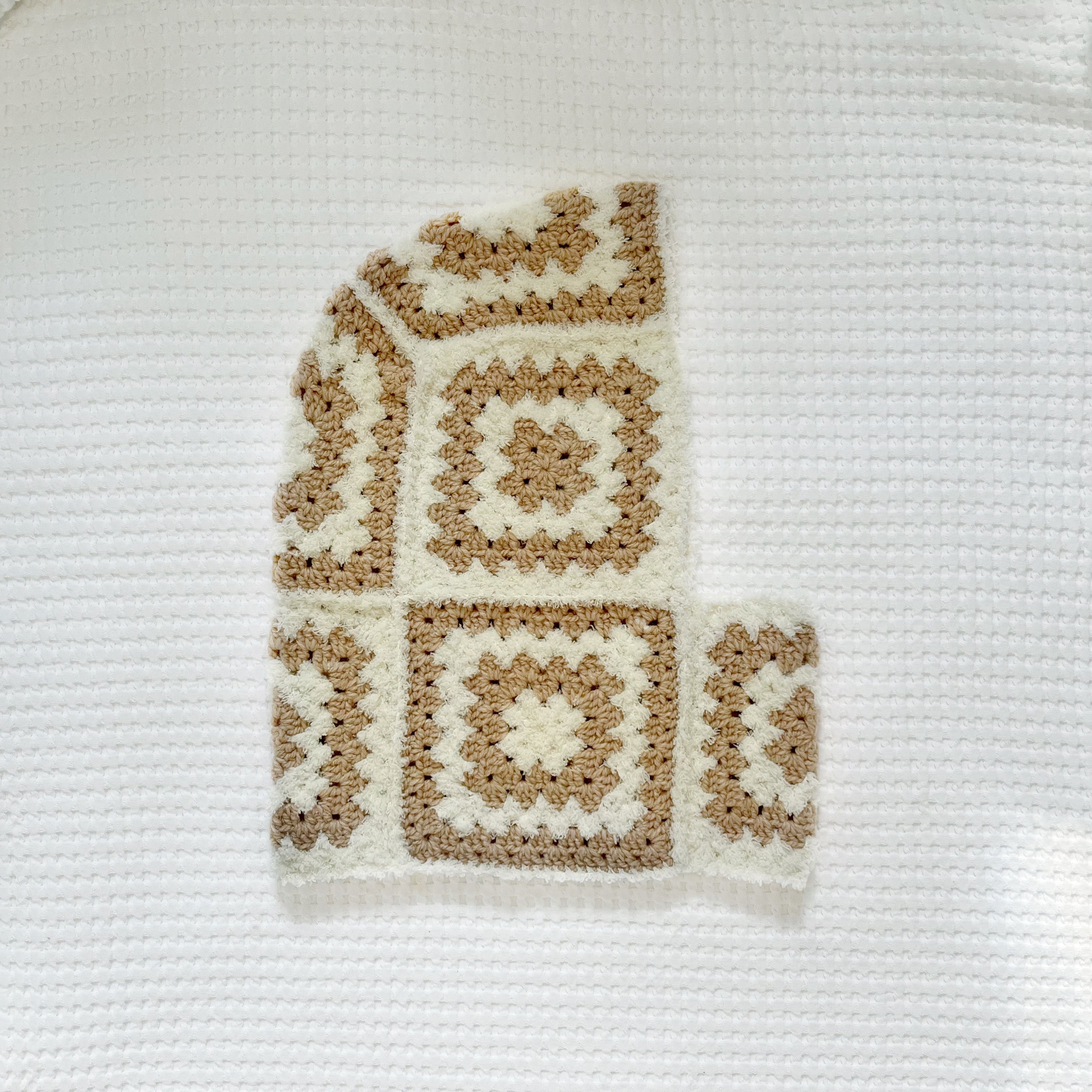 Crocheted balaclava in beige and white colors on a textured white background