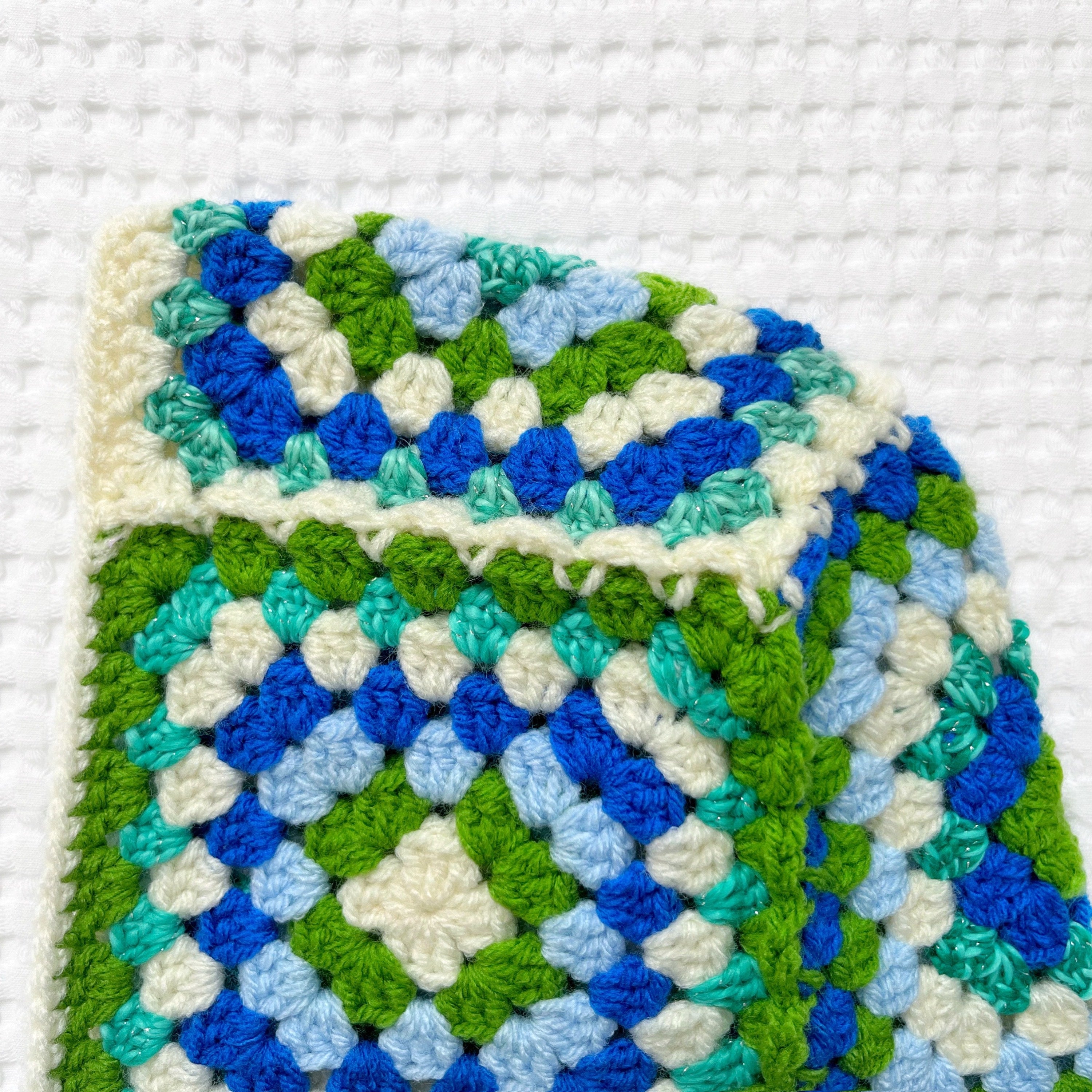 Crocheted balaclava with a geometric pattern in green, blue, and white on a white background