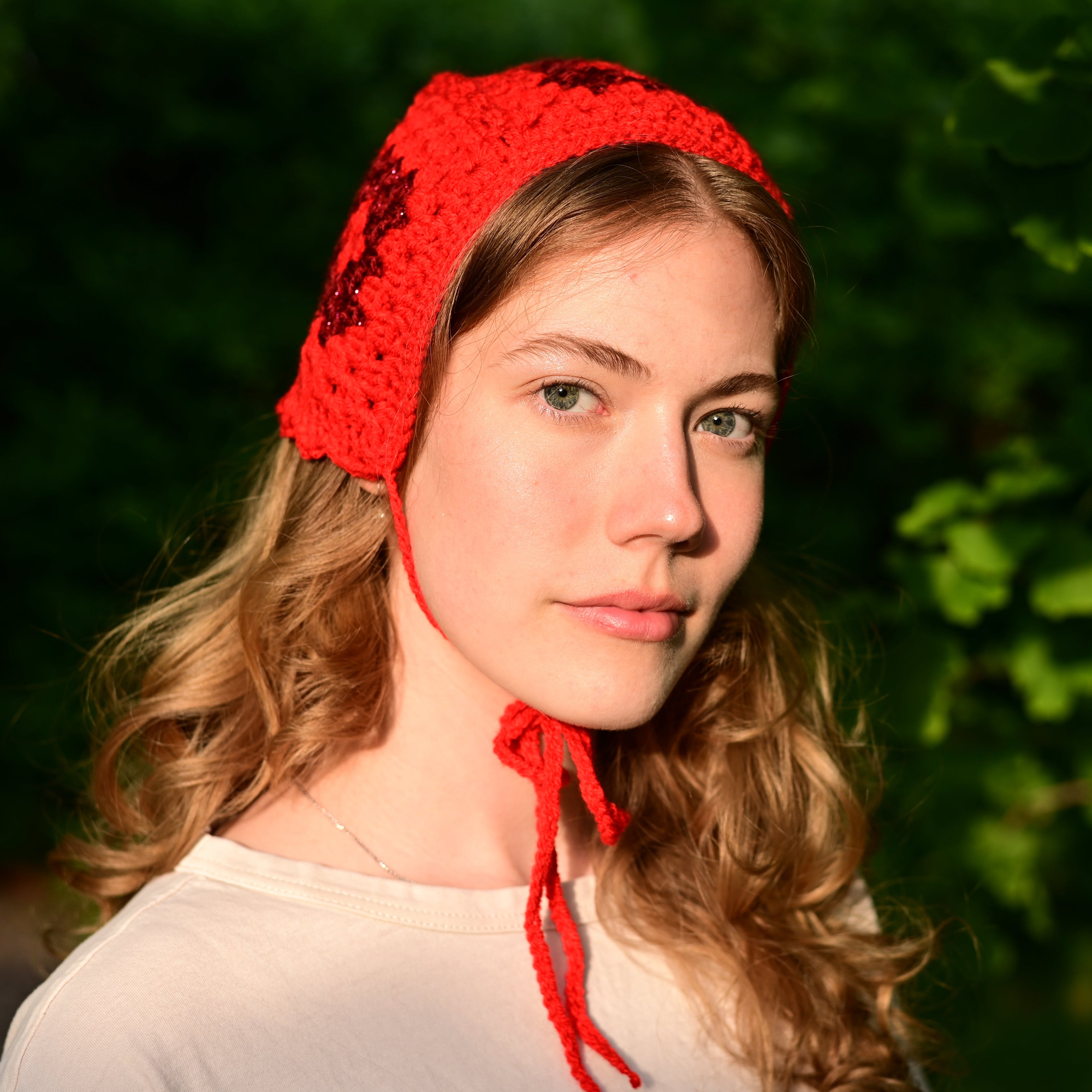 Woman wearing a red crochet bonnet against a green leafy background