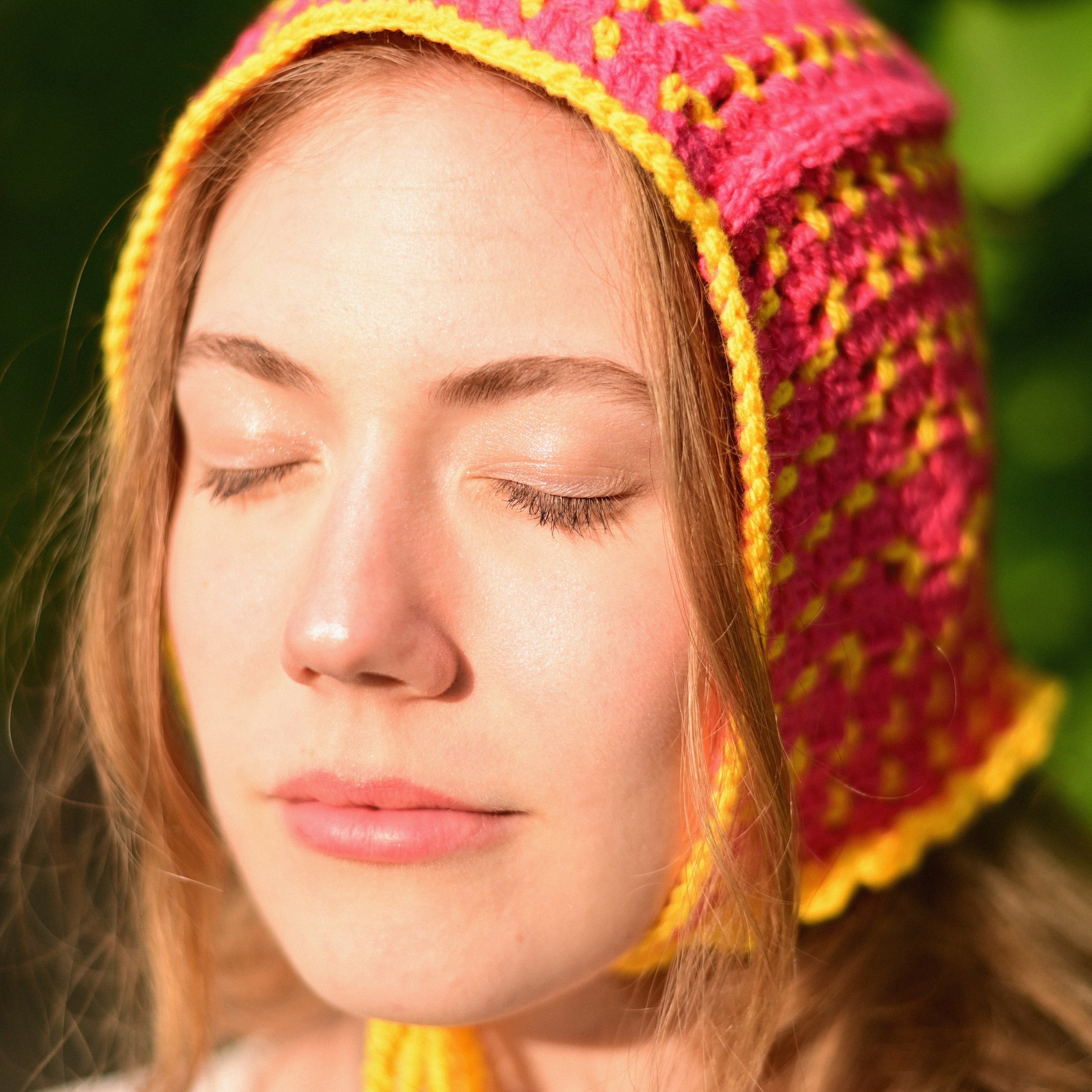 Person wearing a colorful crochetedbonnet with a blurred green background