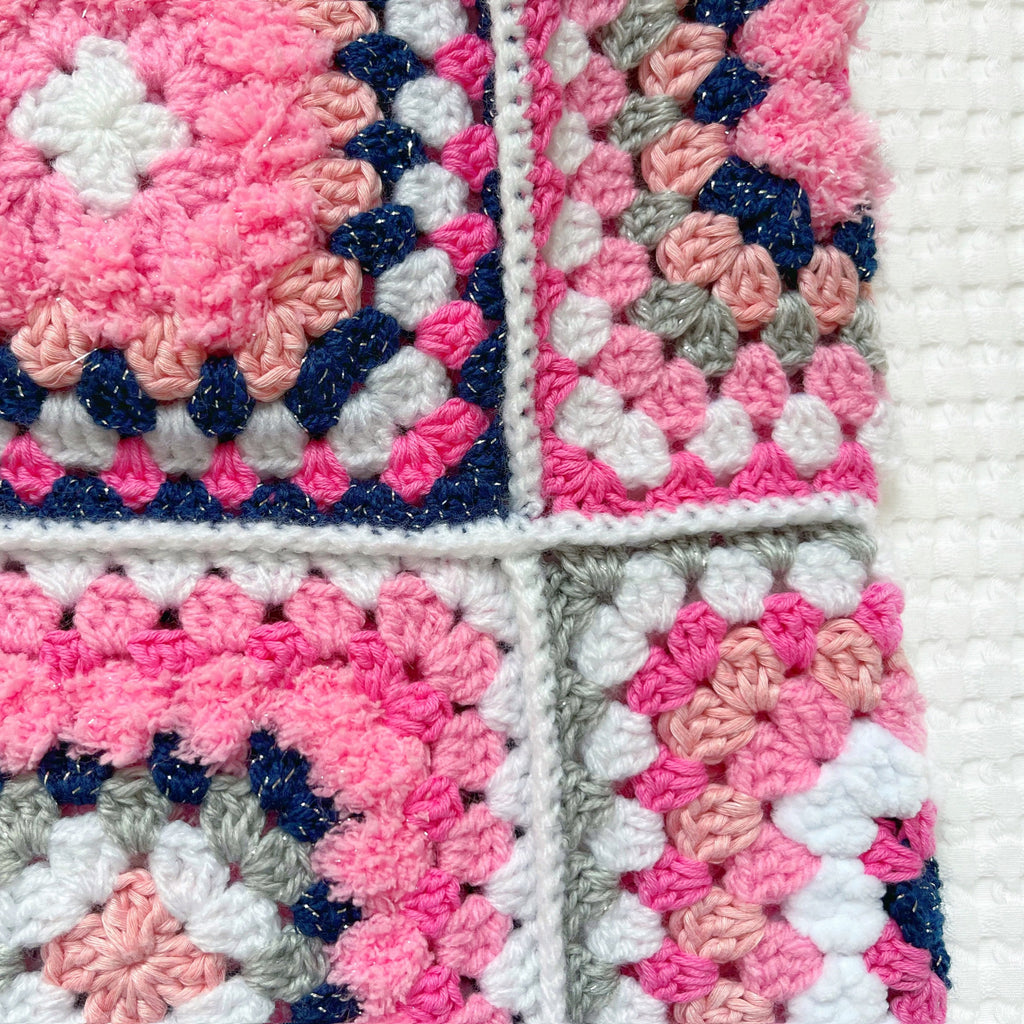 Close-up of a crocheted balaclava with pink, blue, and white squares.