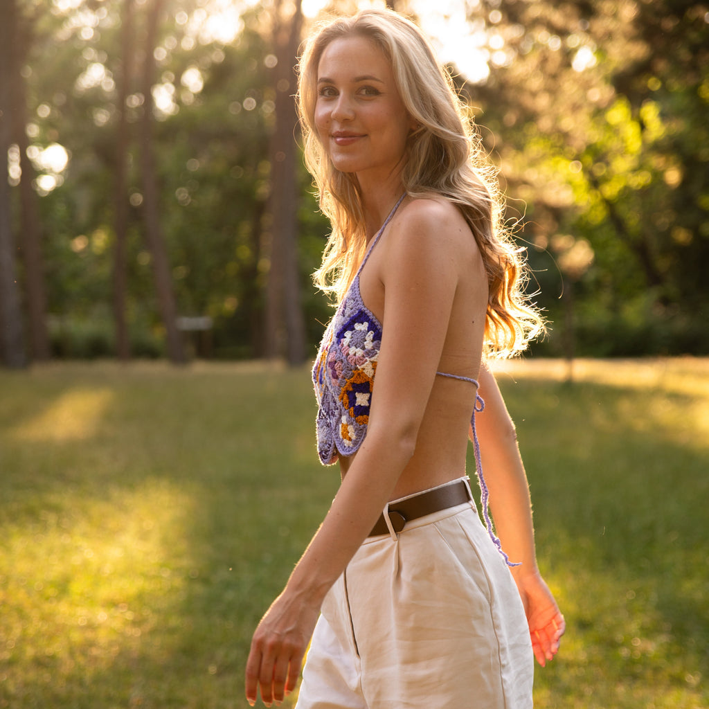 Woman walking in a purple crochet top in a park with trees and sunlight filtering through