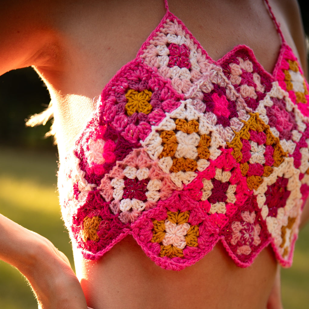 Person wearing a pink crochet top with floral patterns in an outdoor setting