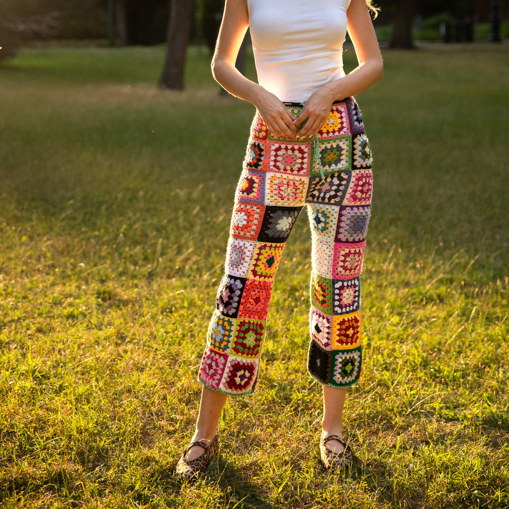 Woman wearing colorful crochet pants standing in a grassy field.