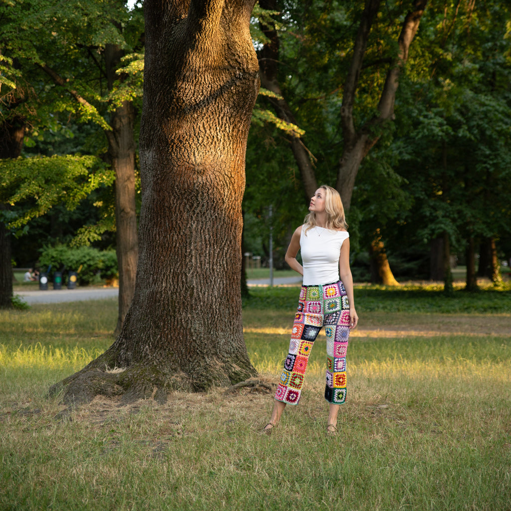 Woman standing next to a large tree in a park in a colorful crochet pants