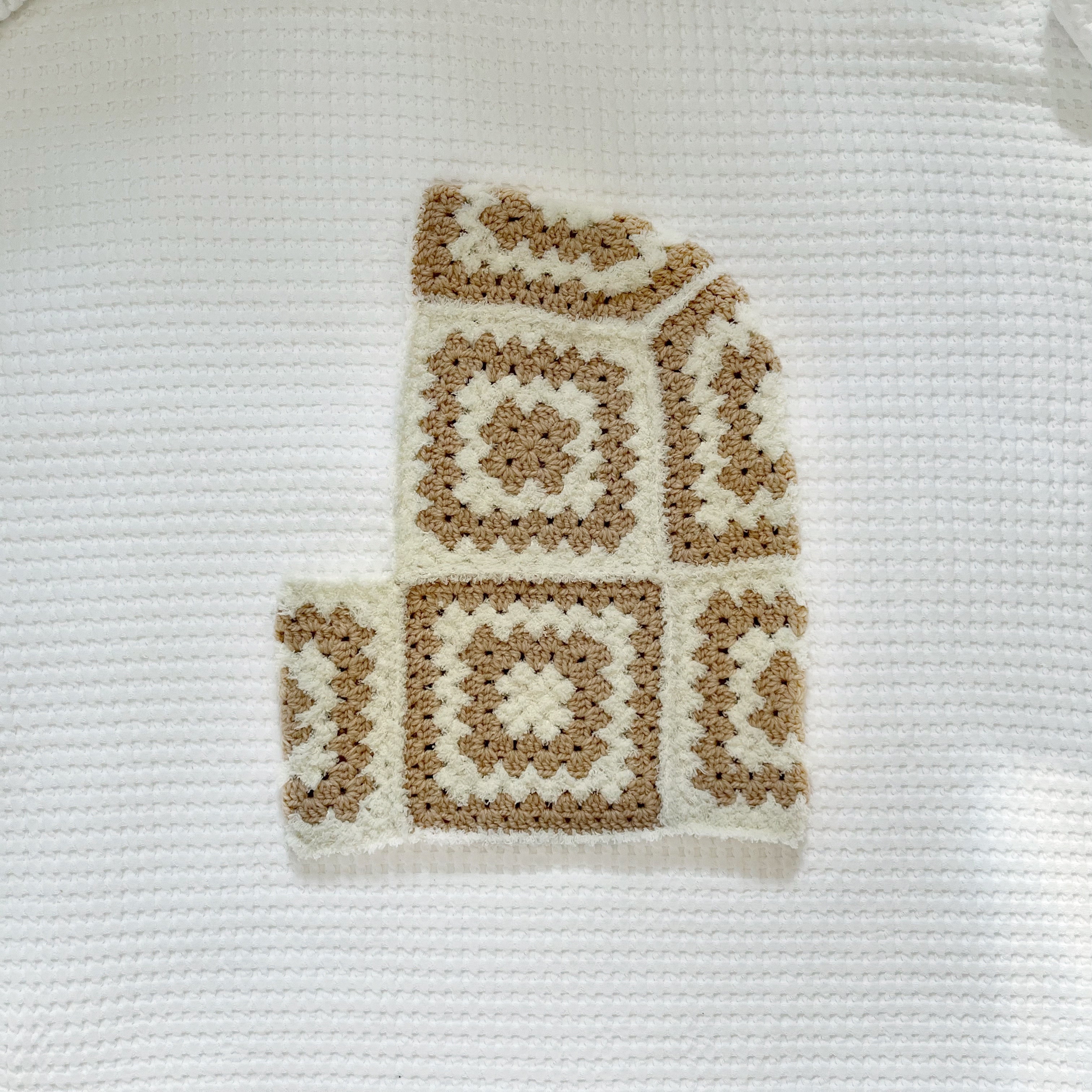 Crocheted balaclava in beige and white colors on a textured white background