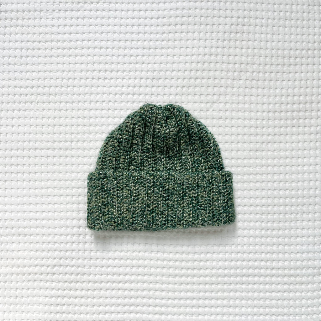 Green metallic crochet beanie on a textured white background