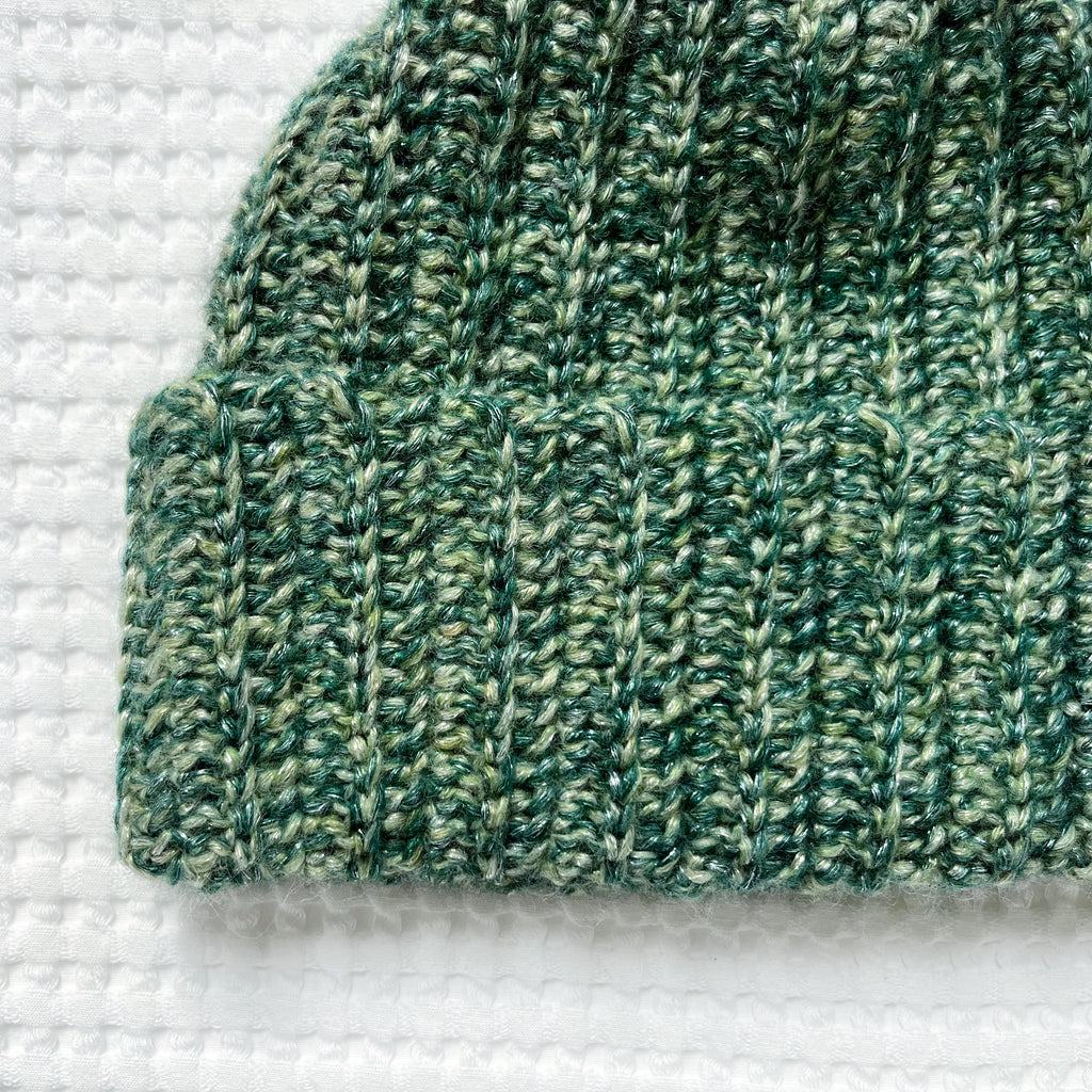 Green metallic crochet beanie on a textured white background