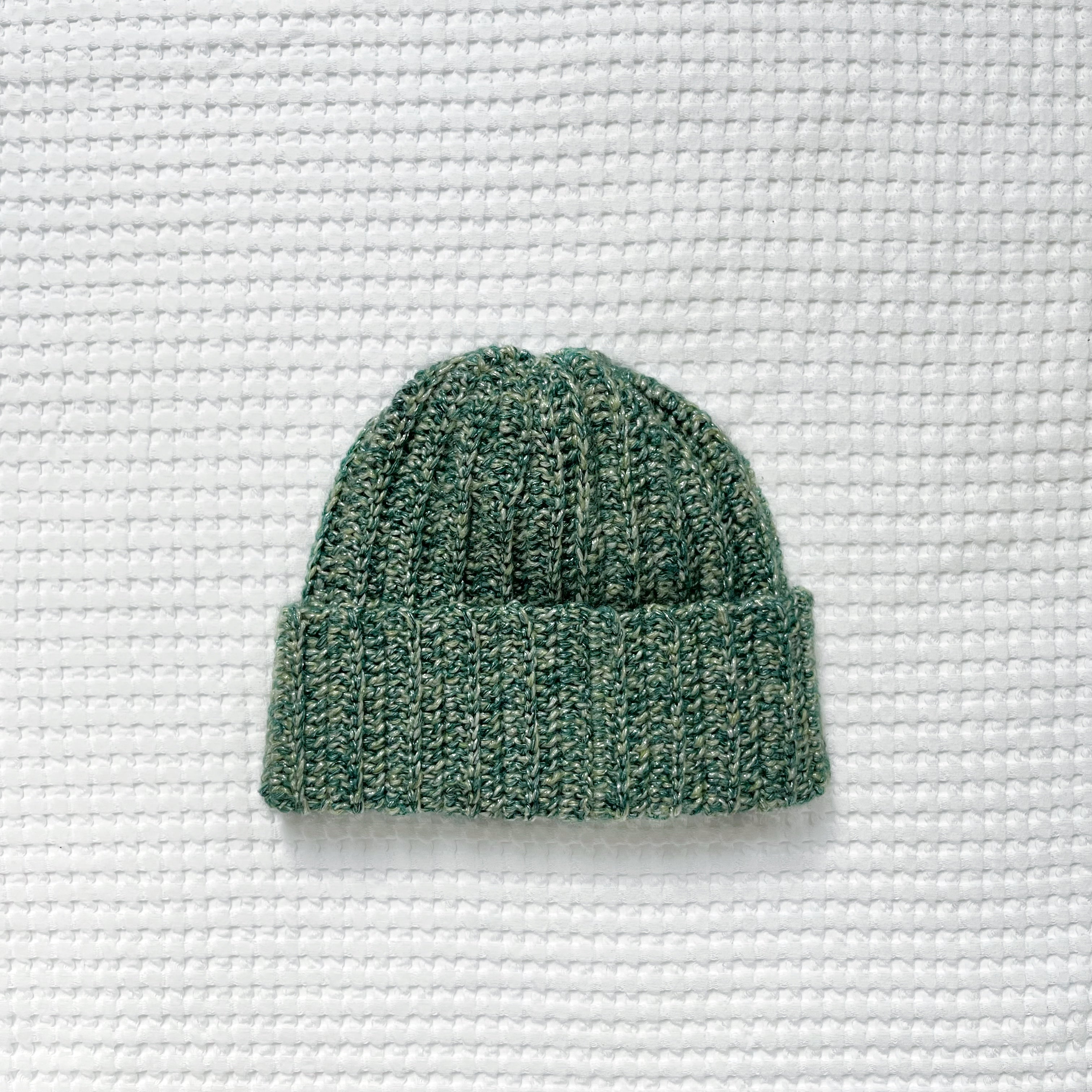 Green metallic crochet beanie on a textured white background