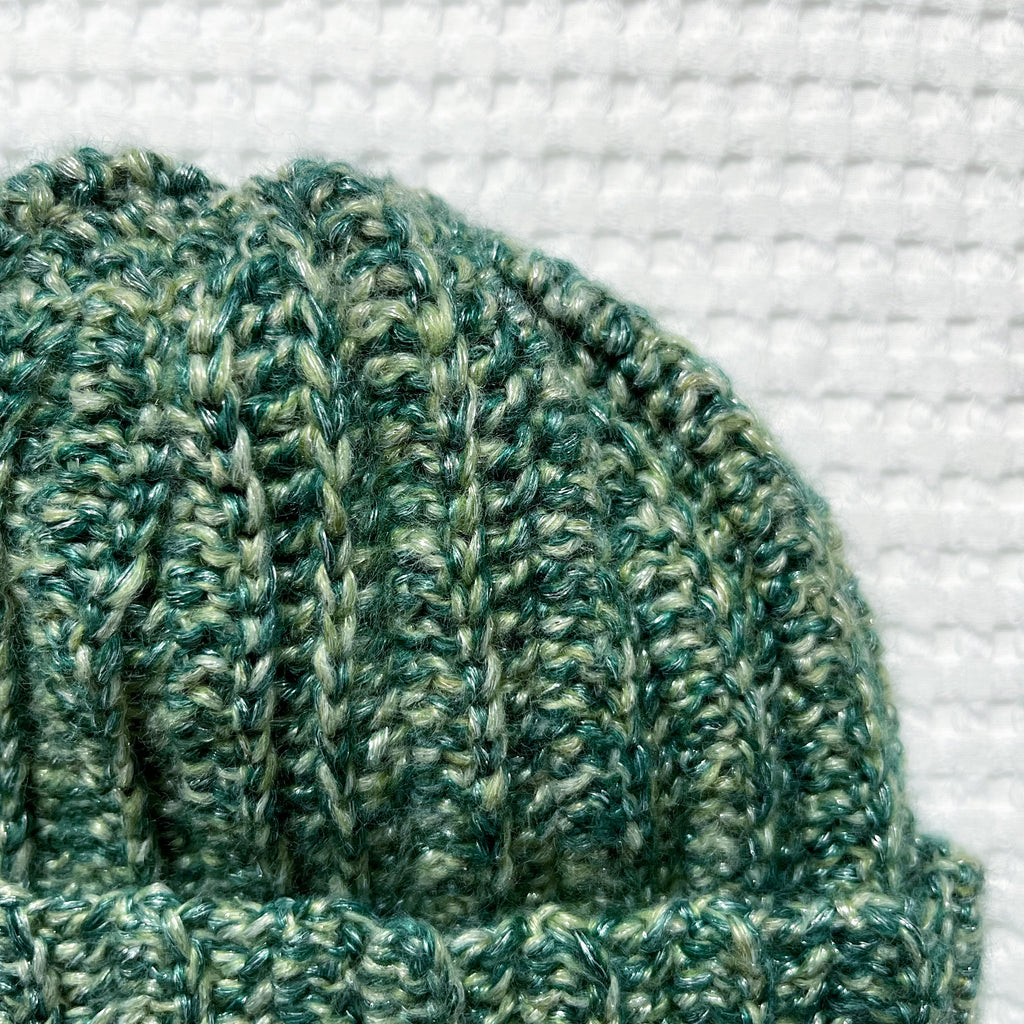 Green metallic crochet beanie on a textured white background