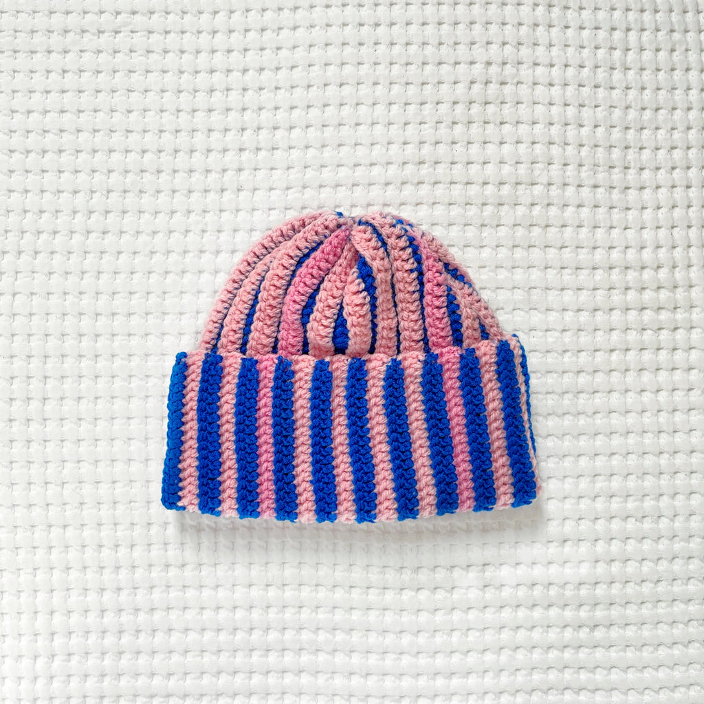 Pink and blue striped crochet beanie on a textured white background