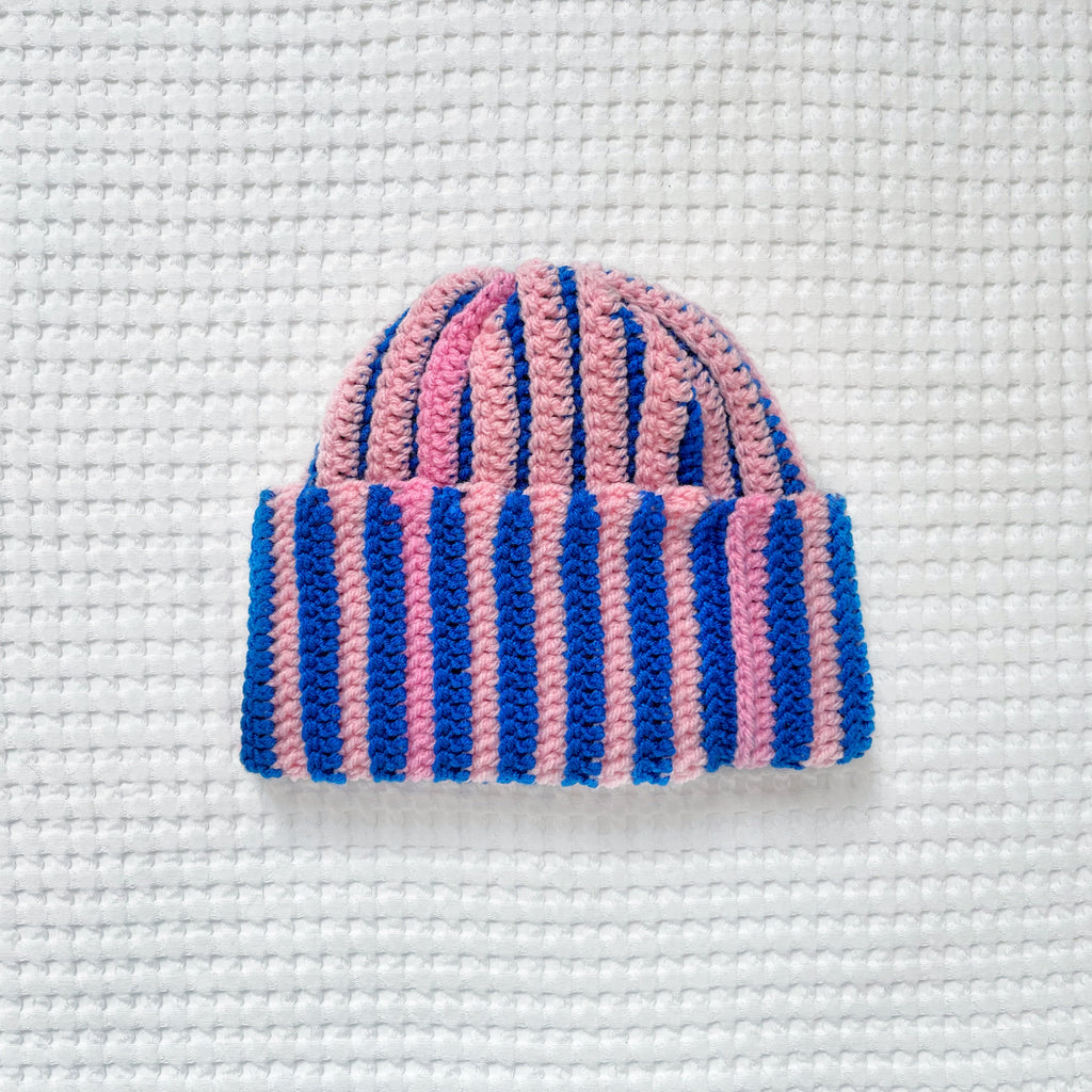 Pink and blue striped crochet beanie on a textured white background