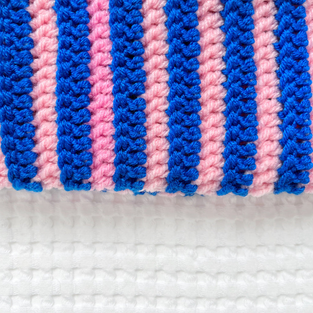 Close-up of a crocheted beanie with pink and blue stripes on a white background