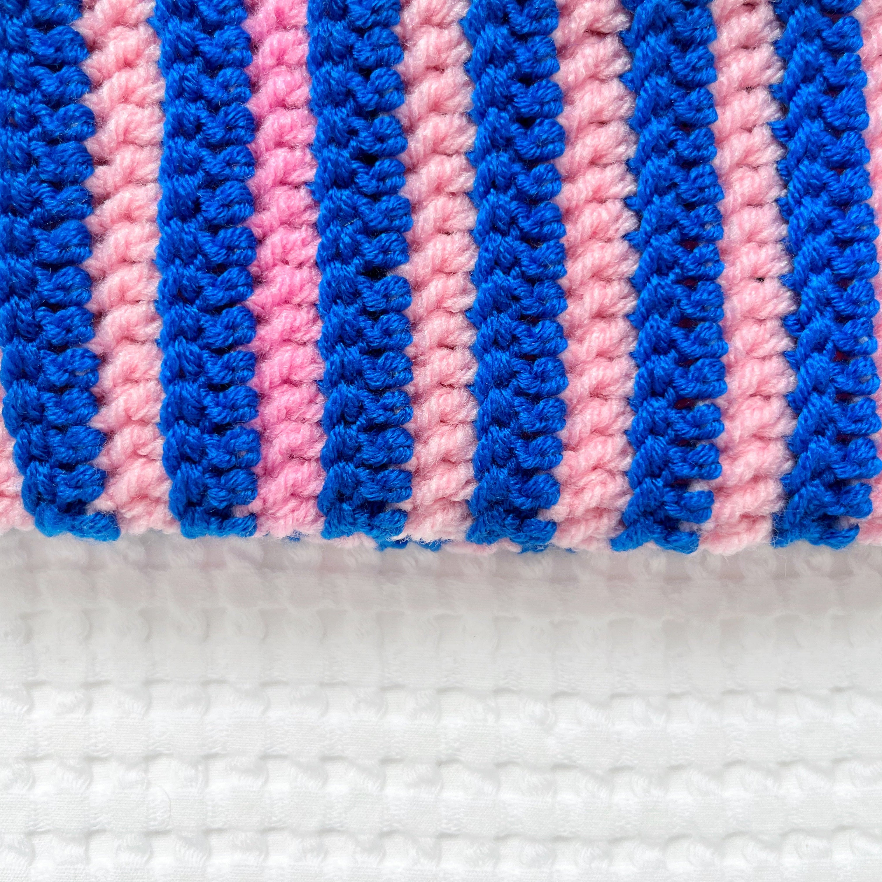 Close-up of a crocheted beanie with pink and blue stripes on a white background