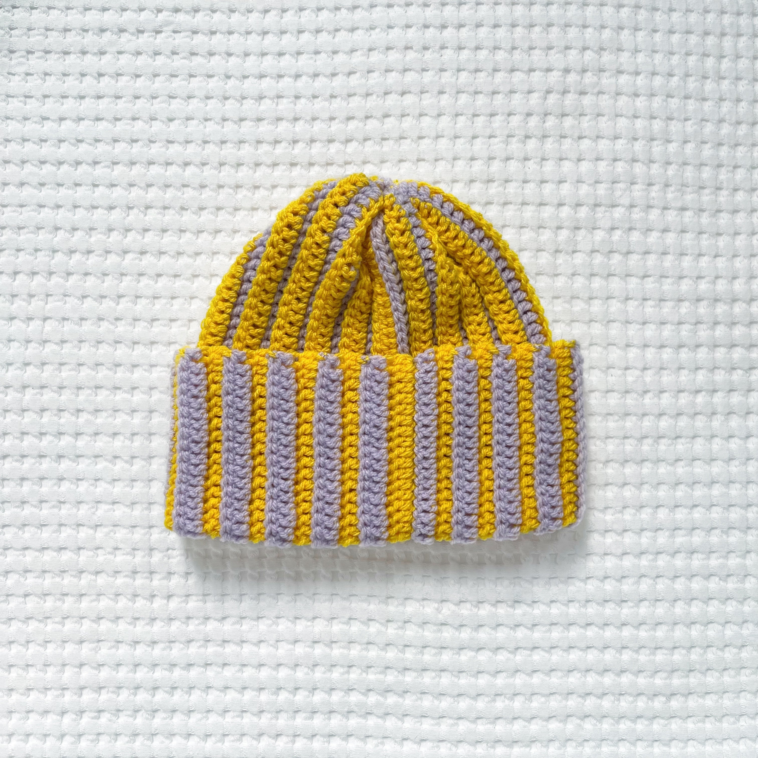 Striped yellow and pastel lilac crochet beanie on a textured white background