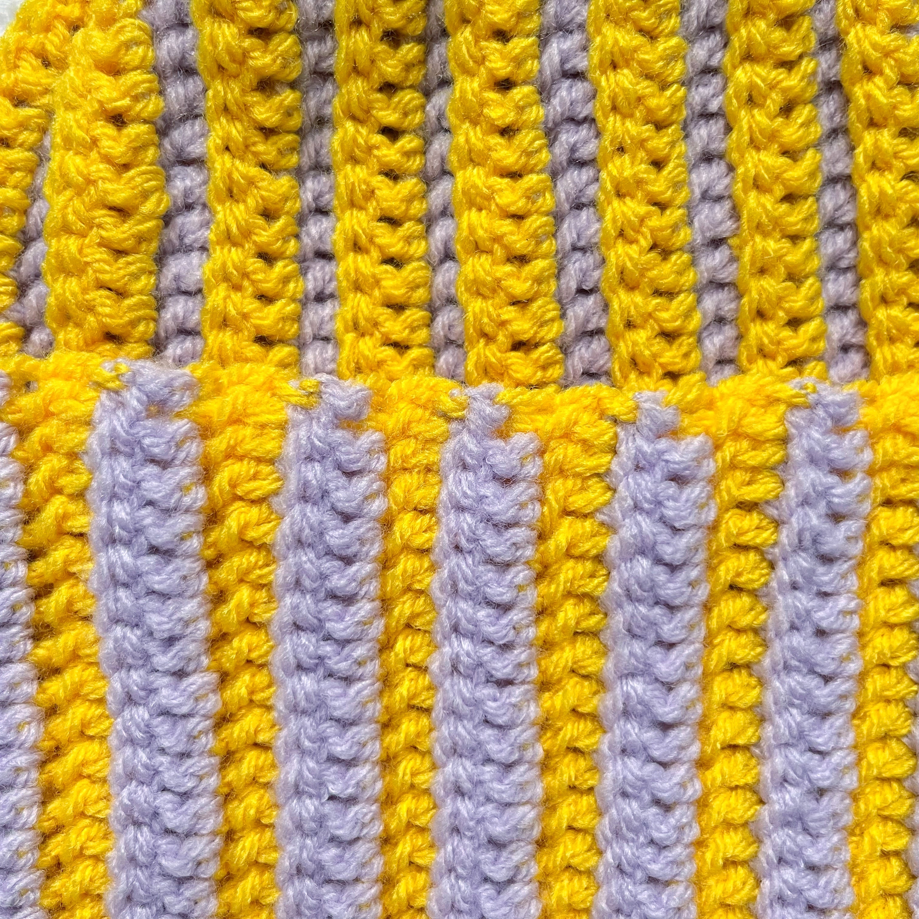 Striped yellow and pastel lilac crochet beanie on a textured white background
