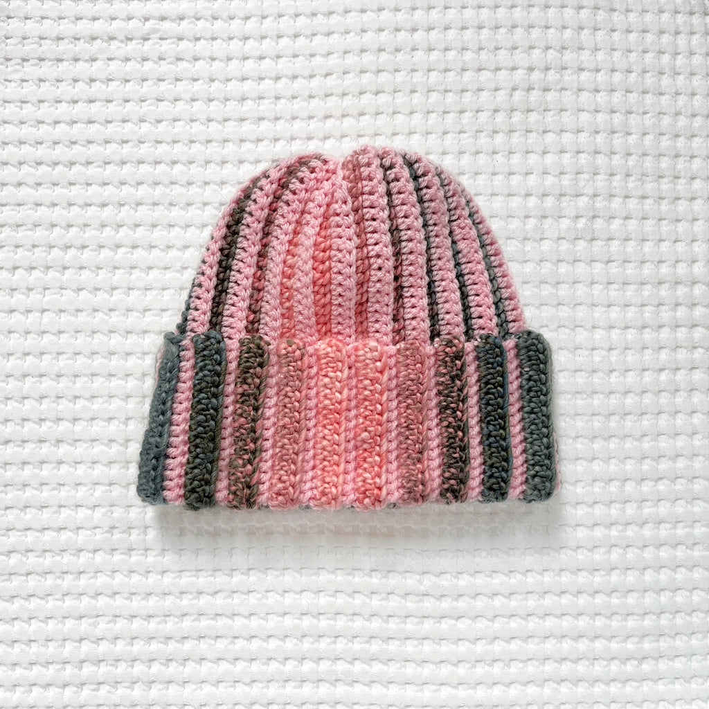 Crocheted pink and green striped beanie on a textured white background
