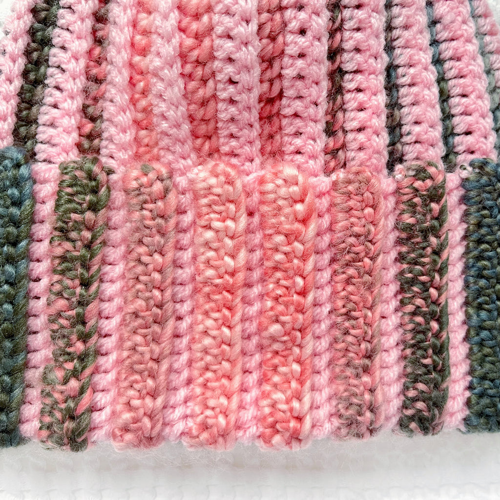 Crocheted pink and green striped beanie on a textured white background