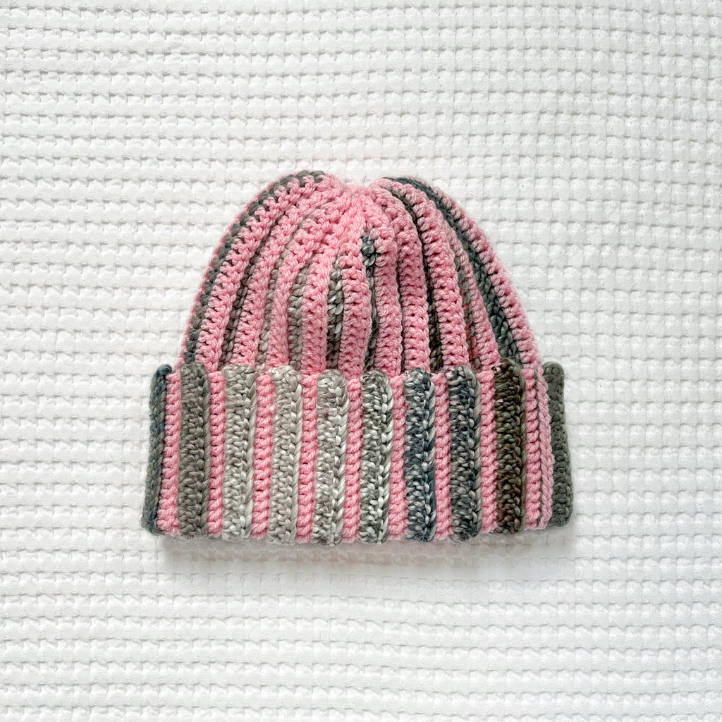 Crocheted pink and green striped beanie on a textured white background