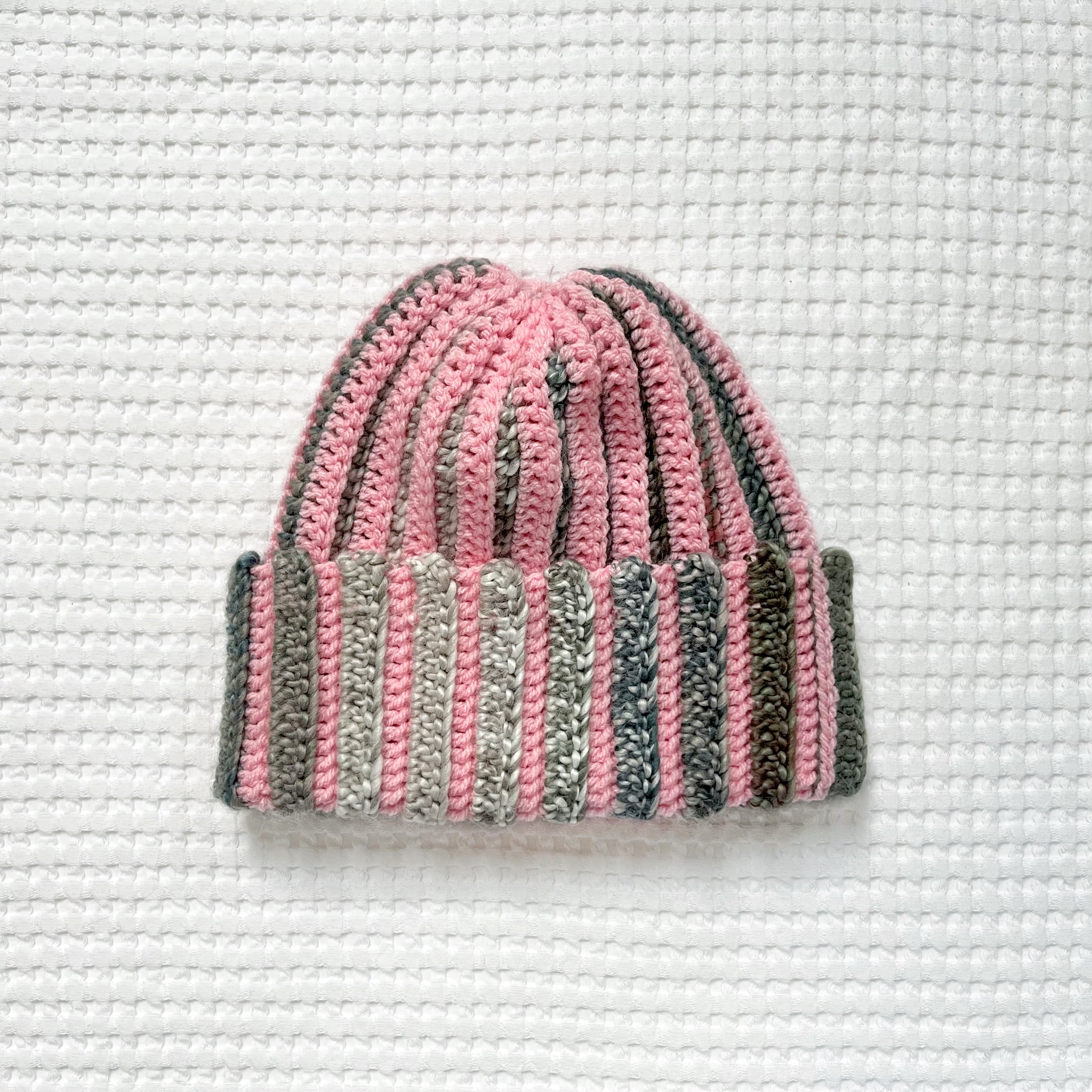 Crocheted pink and green striped beanie on a textured white background