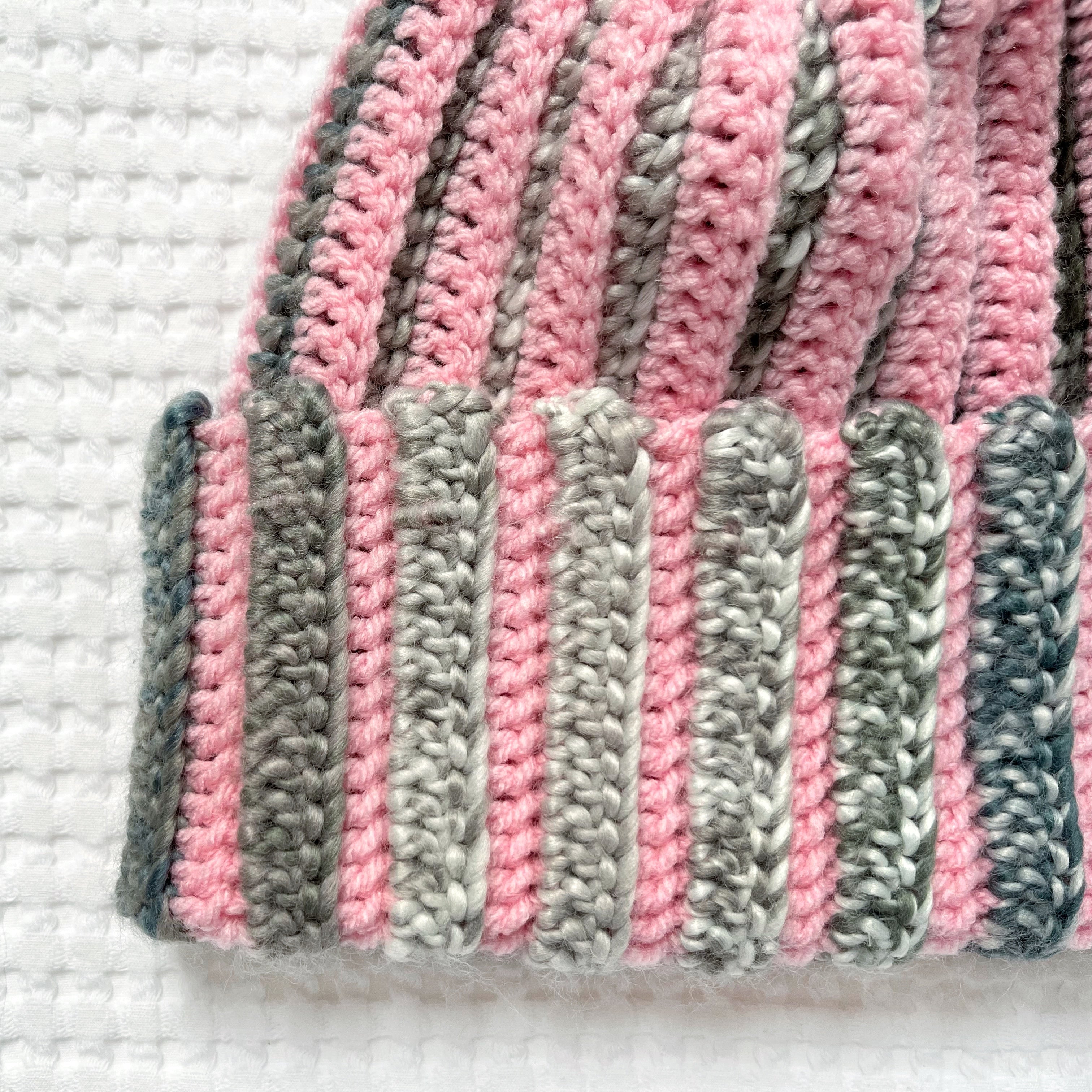 Crocheted pink and green striped beanie on a textured white background