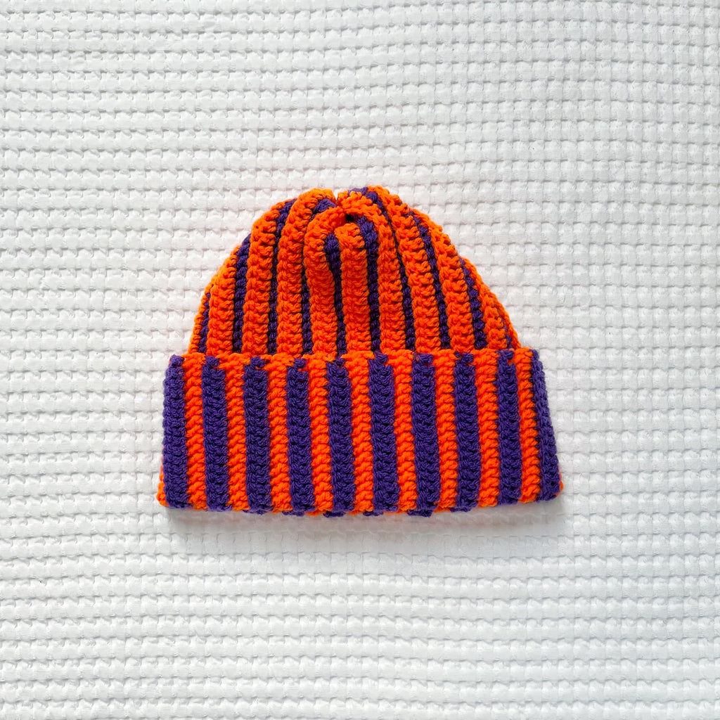 Striped orange and purple crochet beanie on a textured white background