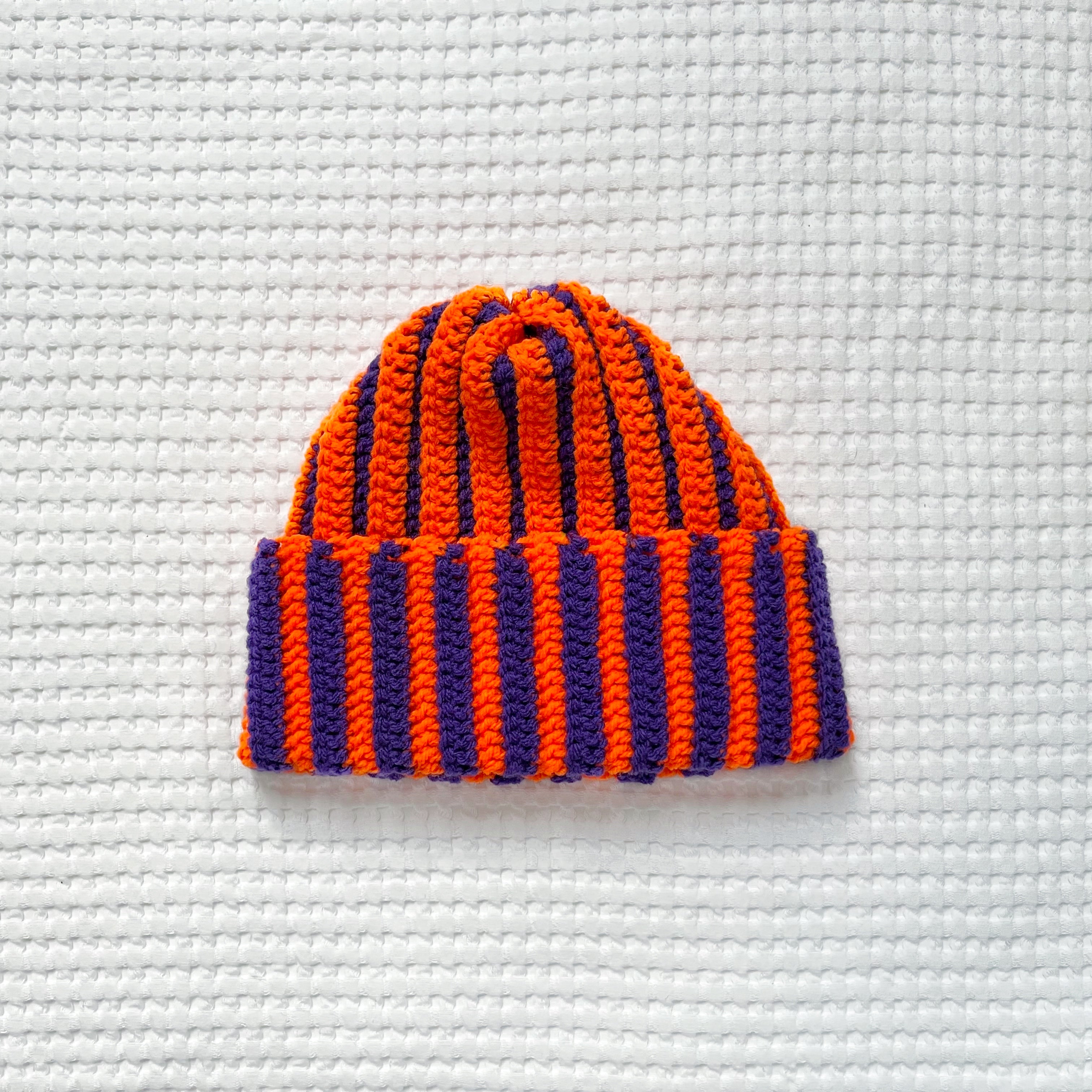 Striped orange and purple crochet beanie on a textured white background