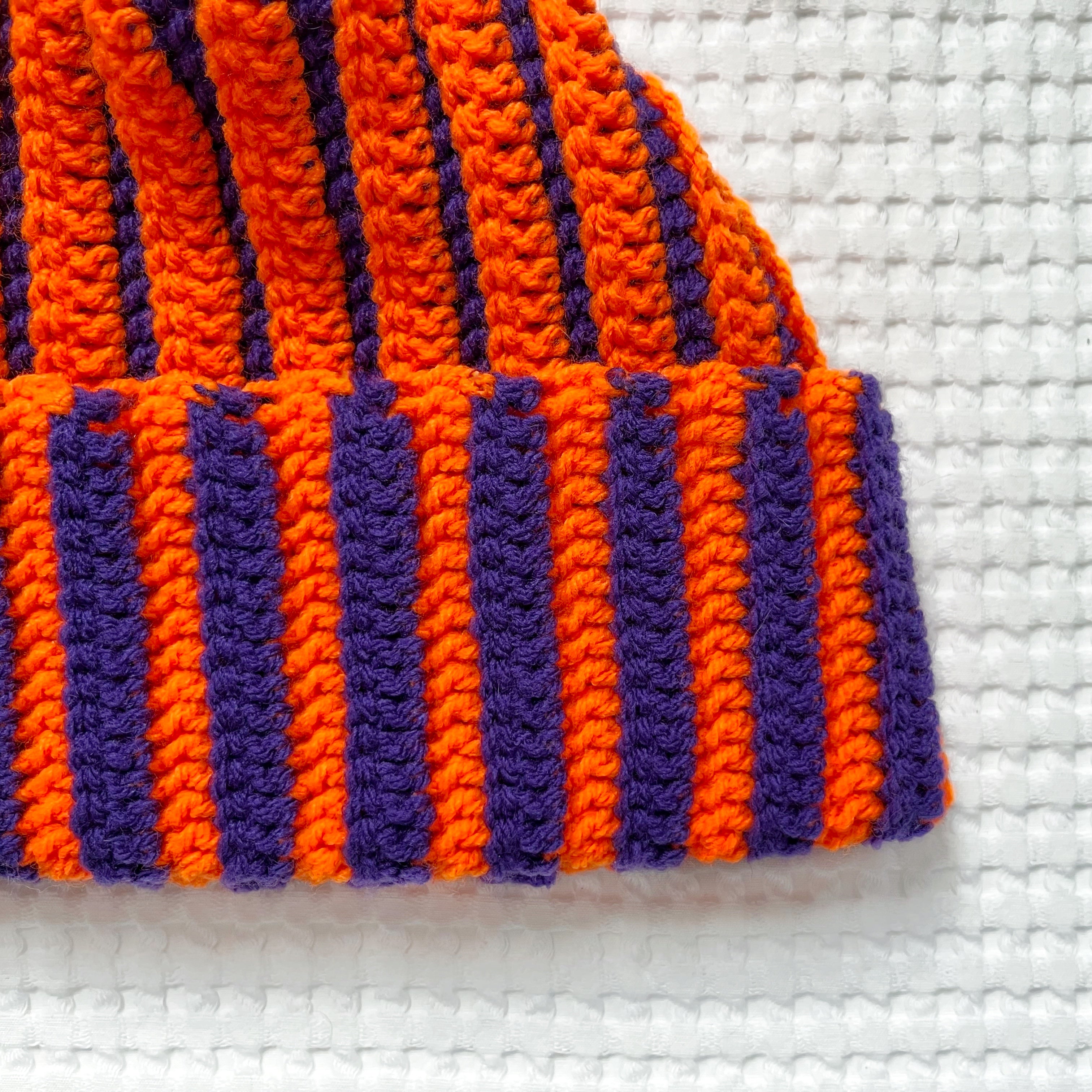 Striped orange and purple crochet beanie on a textured white background