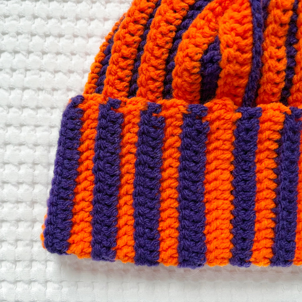 Striped orange and purple crochet beanie on a textured white background