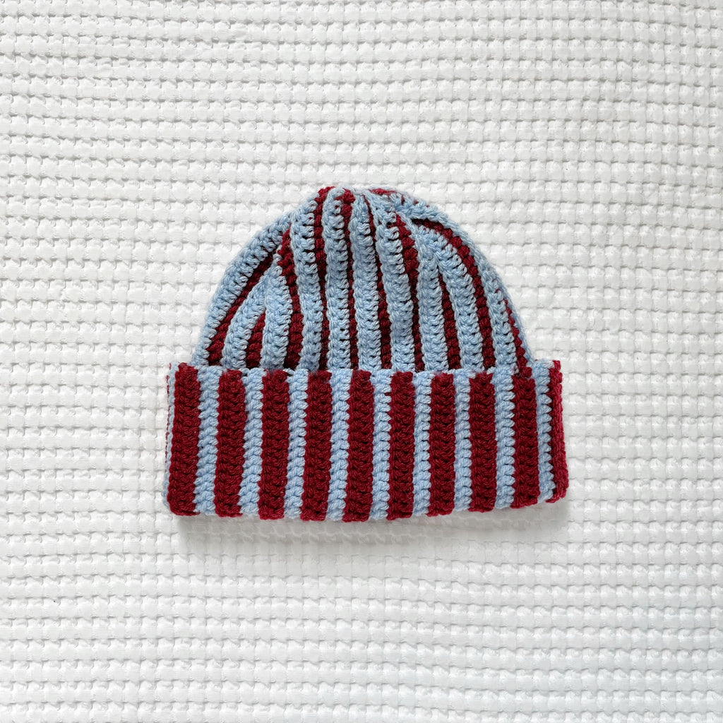Striped crochet burgundy and blue beanie on a textured white background