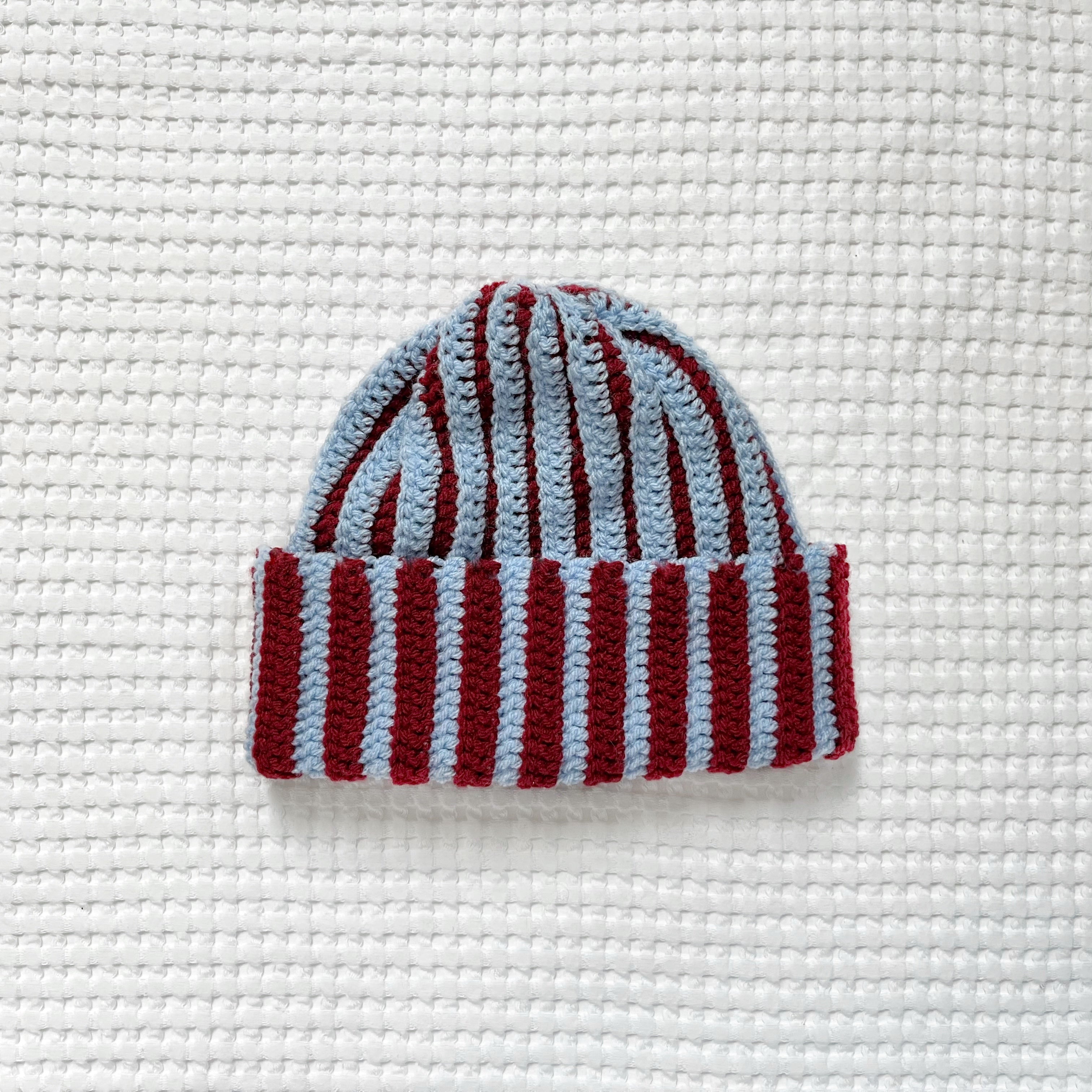 Striped crochet burgundy and blue beanie on a textured white background