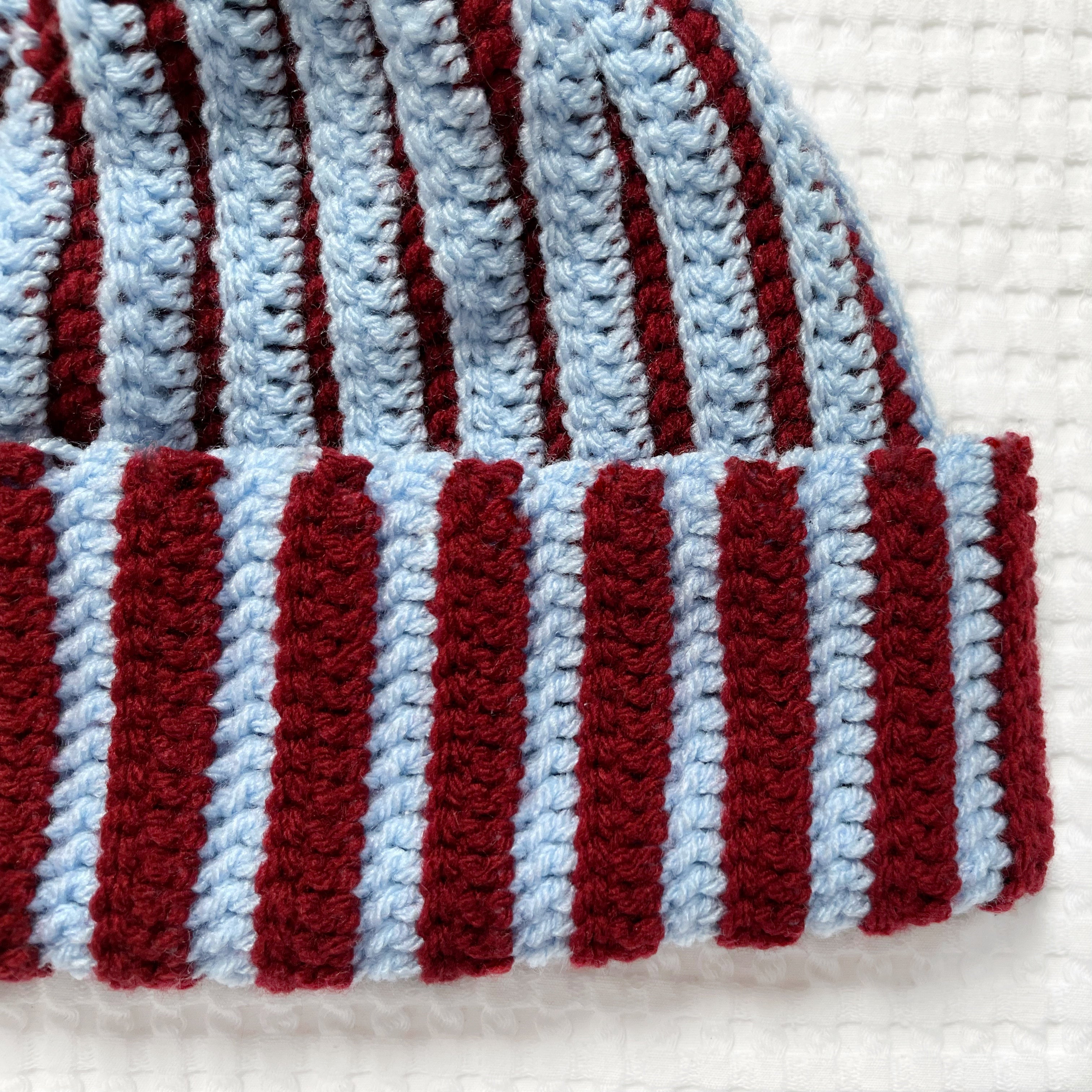 Striped crochet burgundy and blue beanie on a textured white background