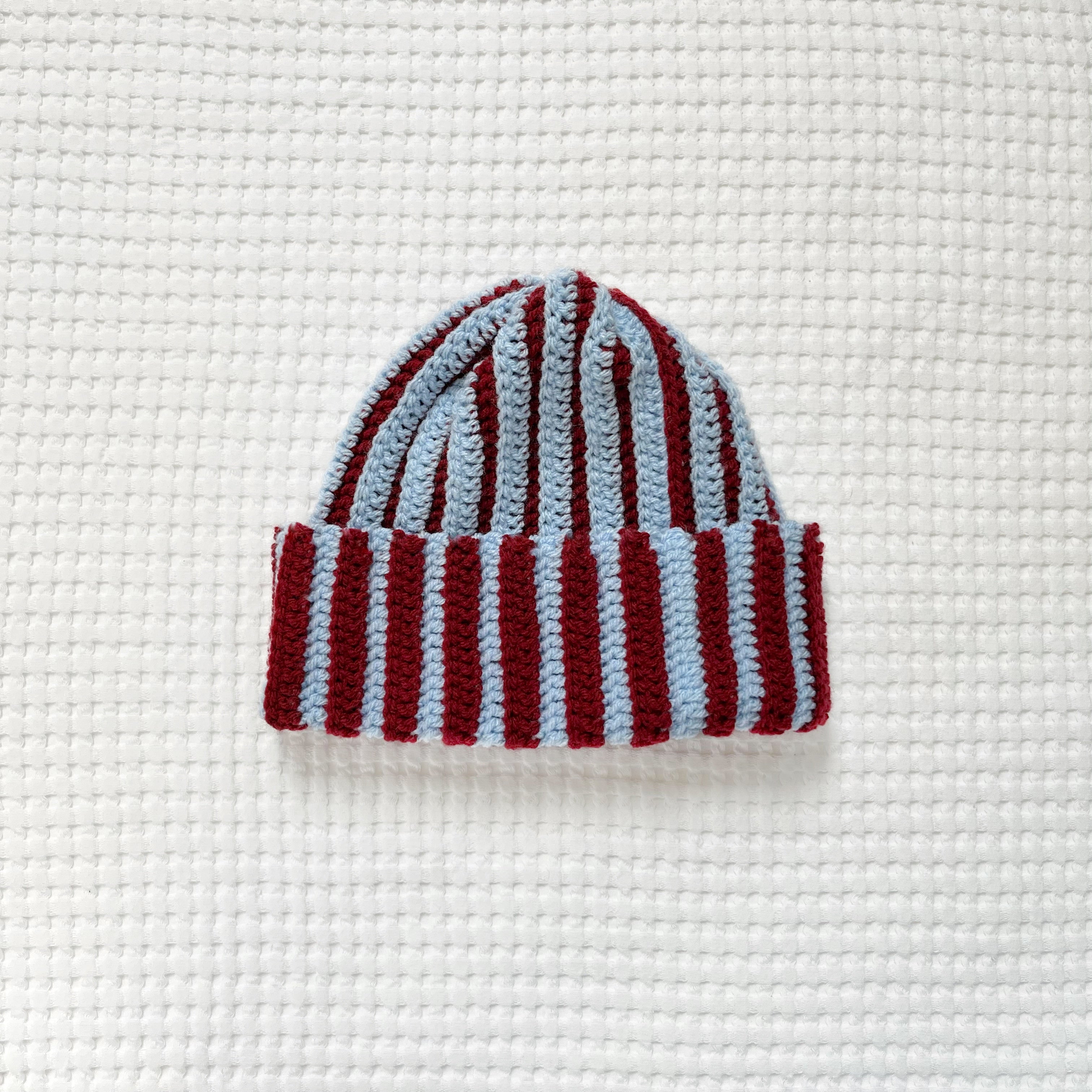 Striped crochet burgundy and blue beanie on a textured white background