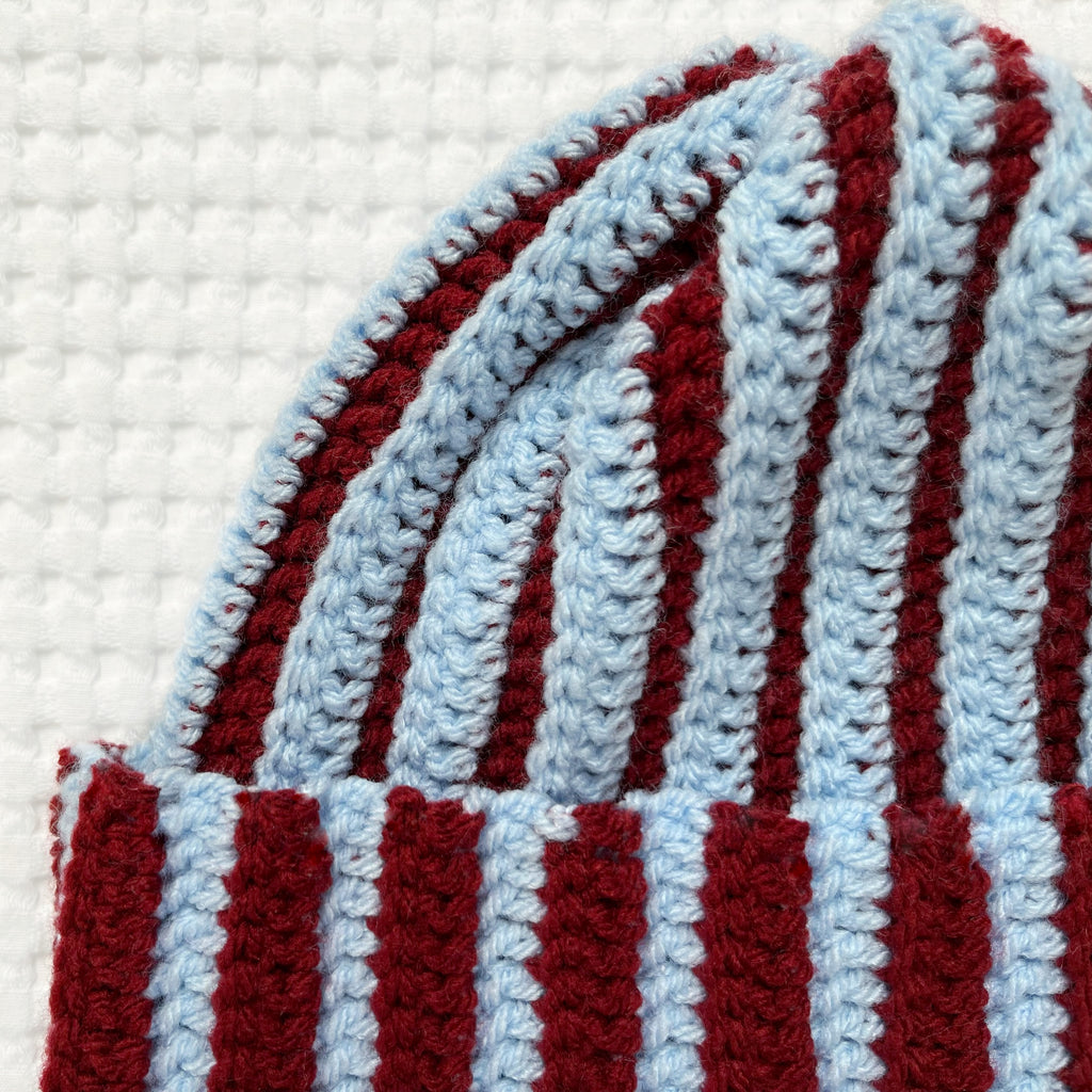 Striped crochet burgundy and blue beanie on a textured white background