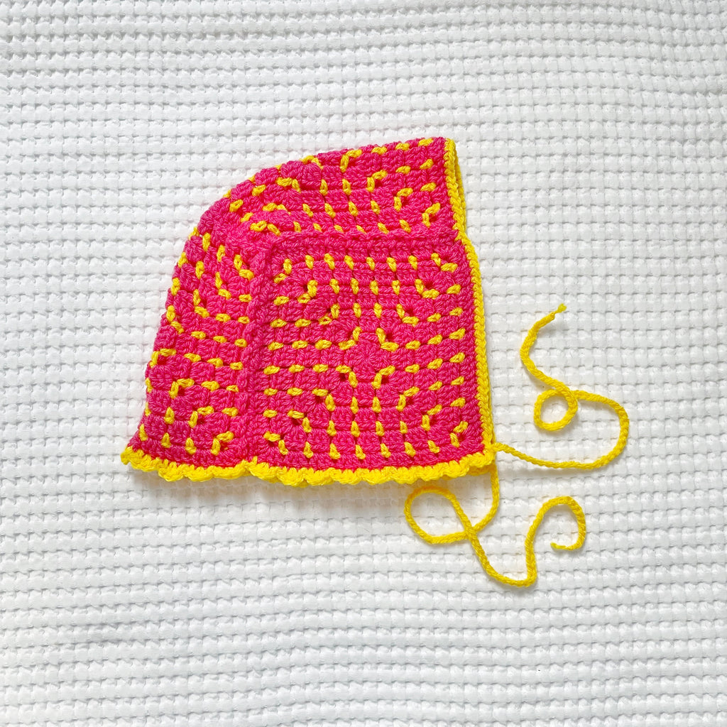 Pink and yellow crocheted bonnet on a white textured background