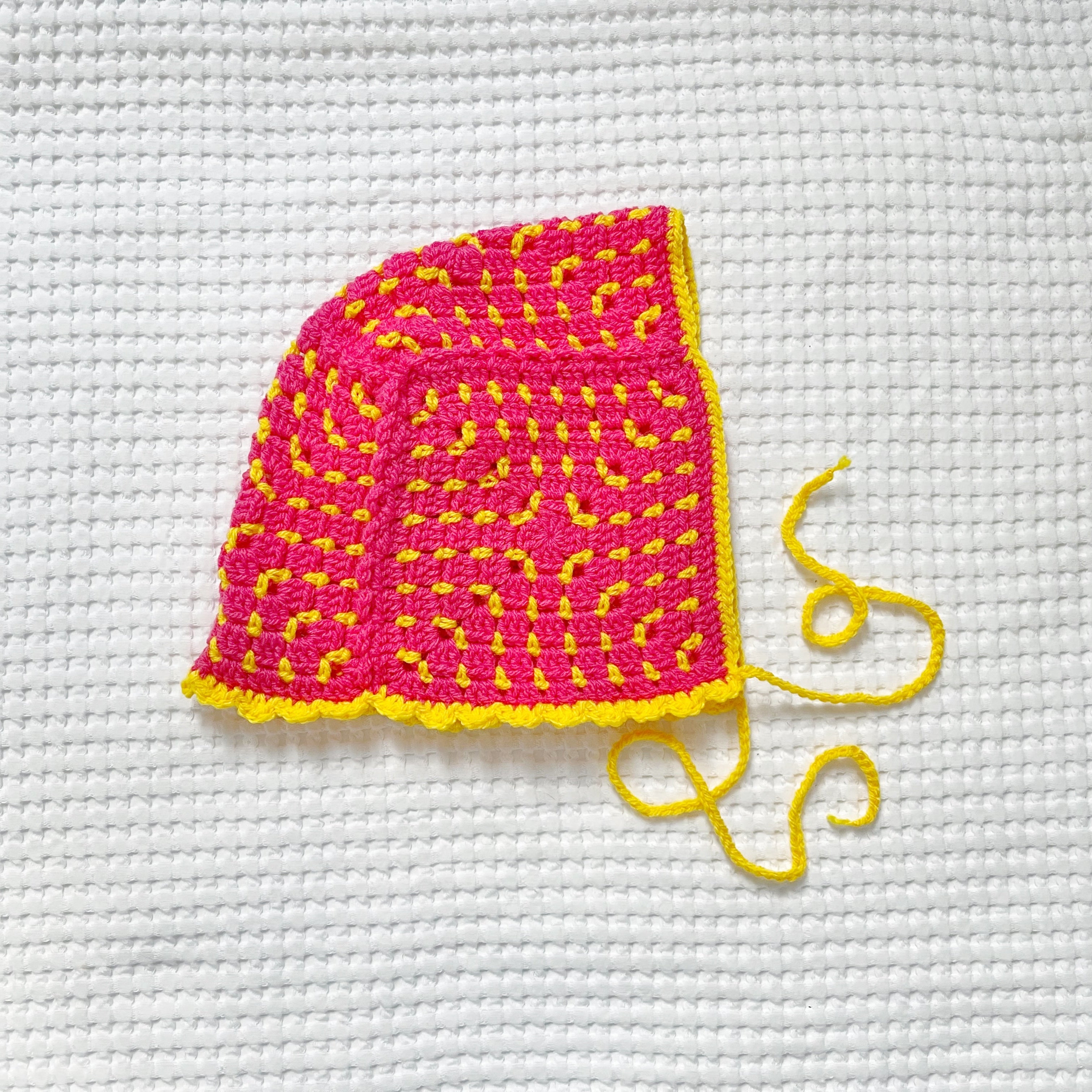 Pink and yellow crocheted bonnet on a white textured background