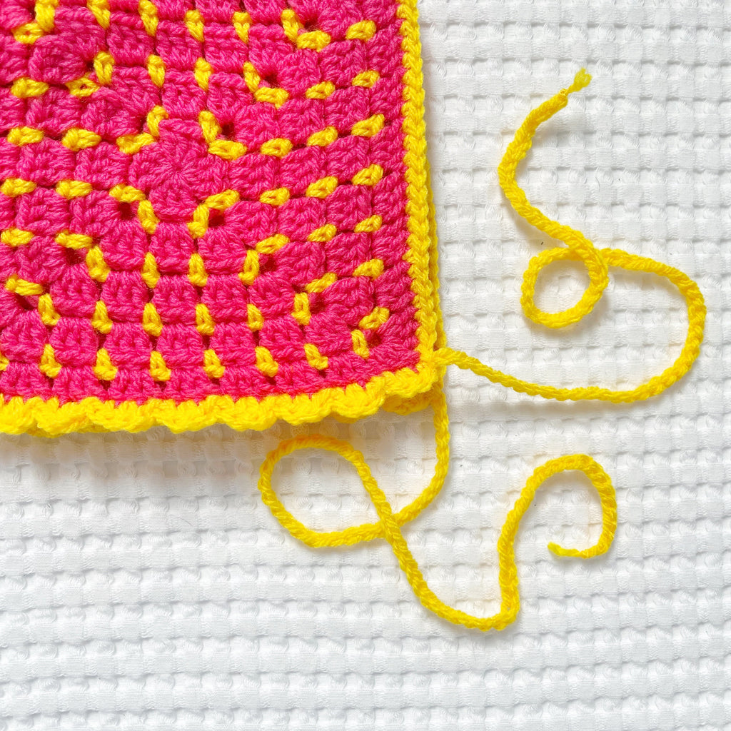 Close-up of a pink and yellow crocheted bonnet on a white background