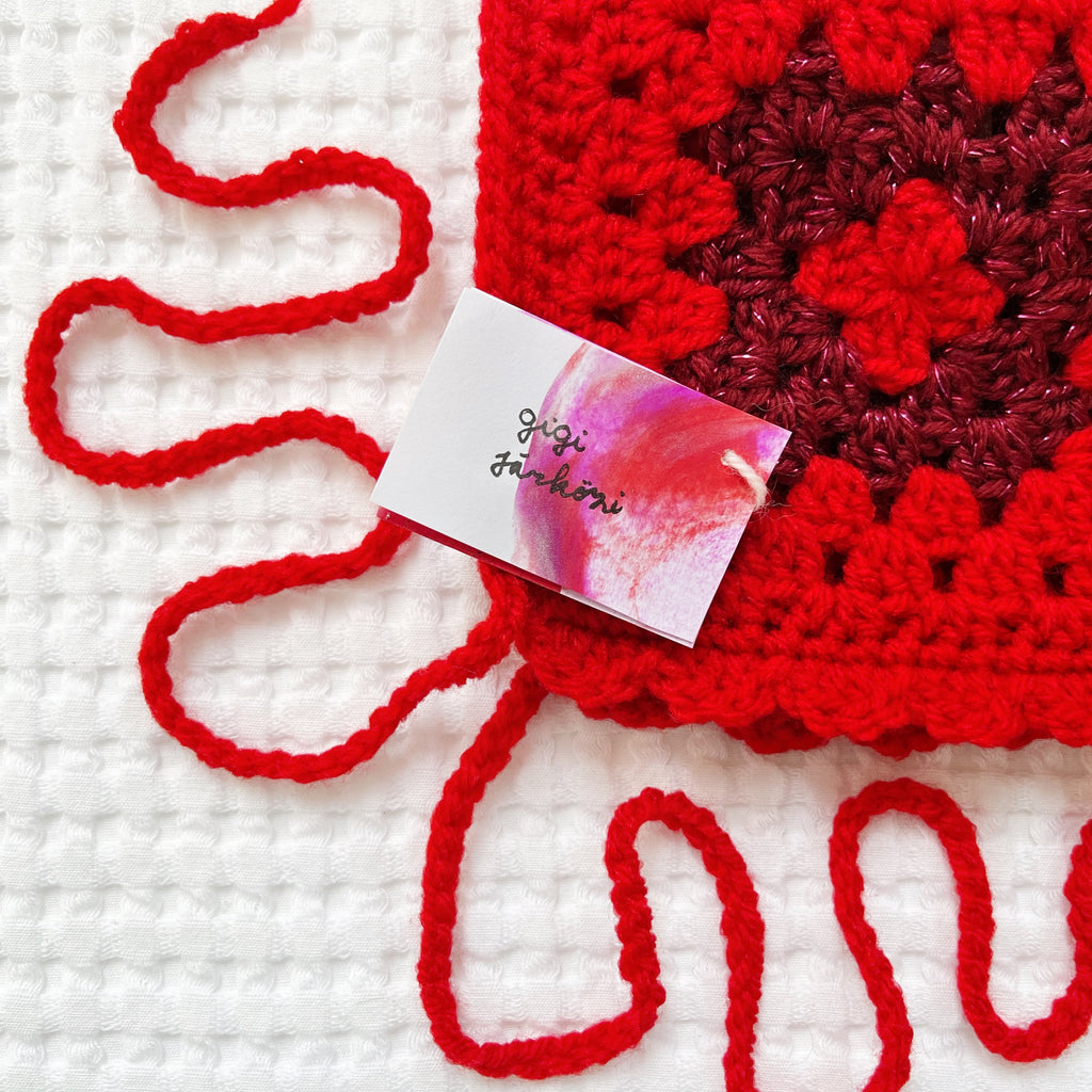 Red crocheted glittery bonnet with a pink card on a white background