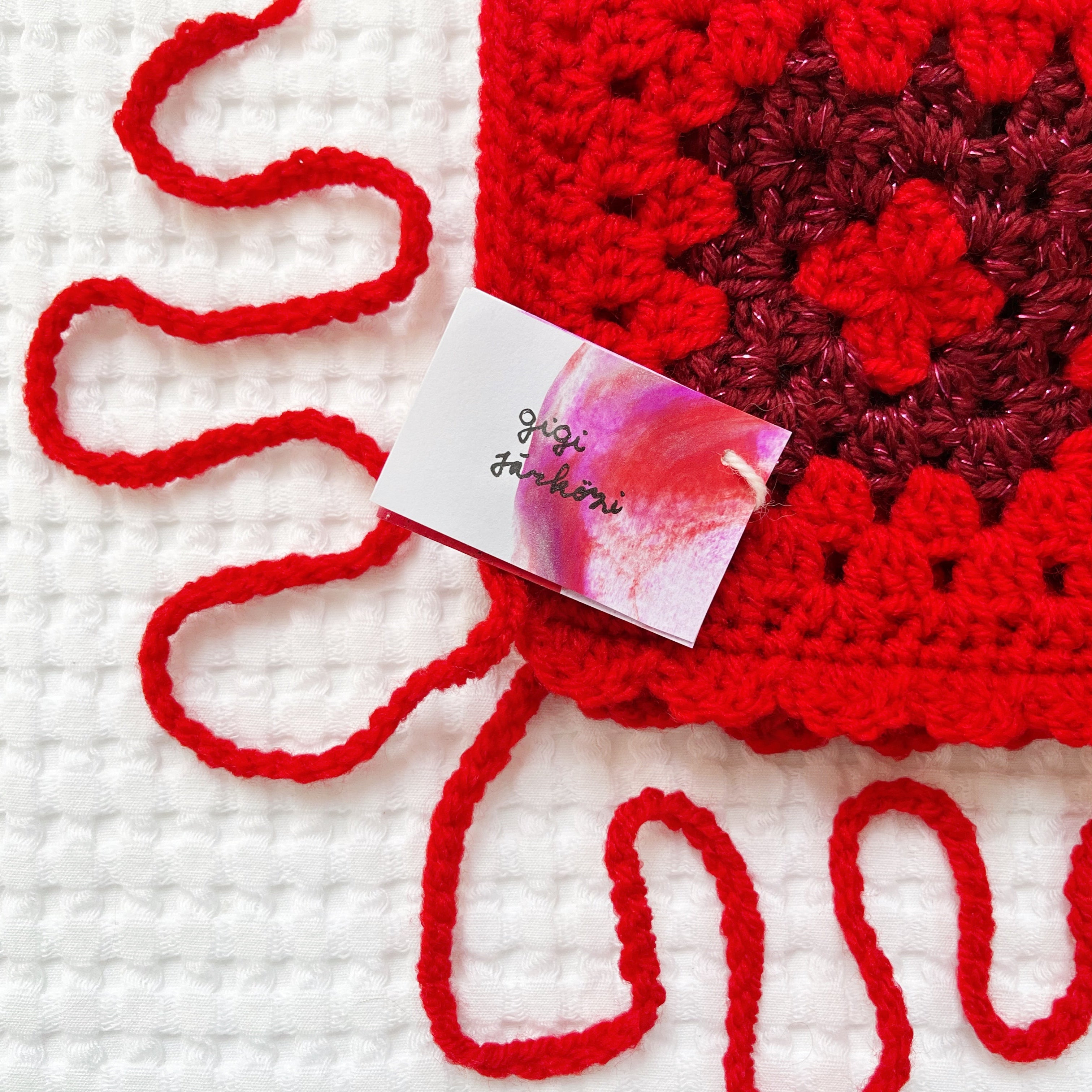 Red crocheted glittery bonnet with a pink card on a white background