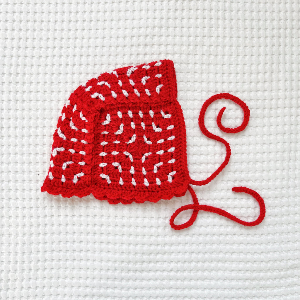 Red crochet bonnet on a white cross-stitched background
