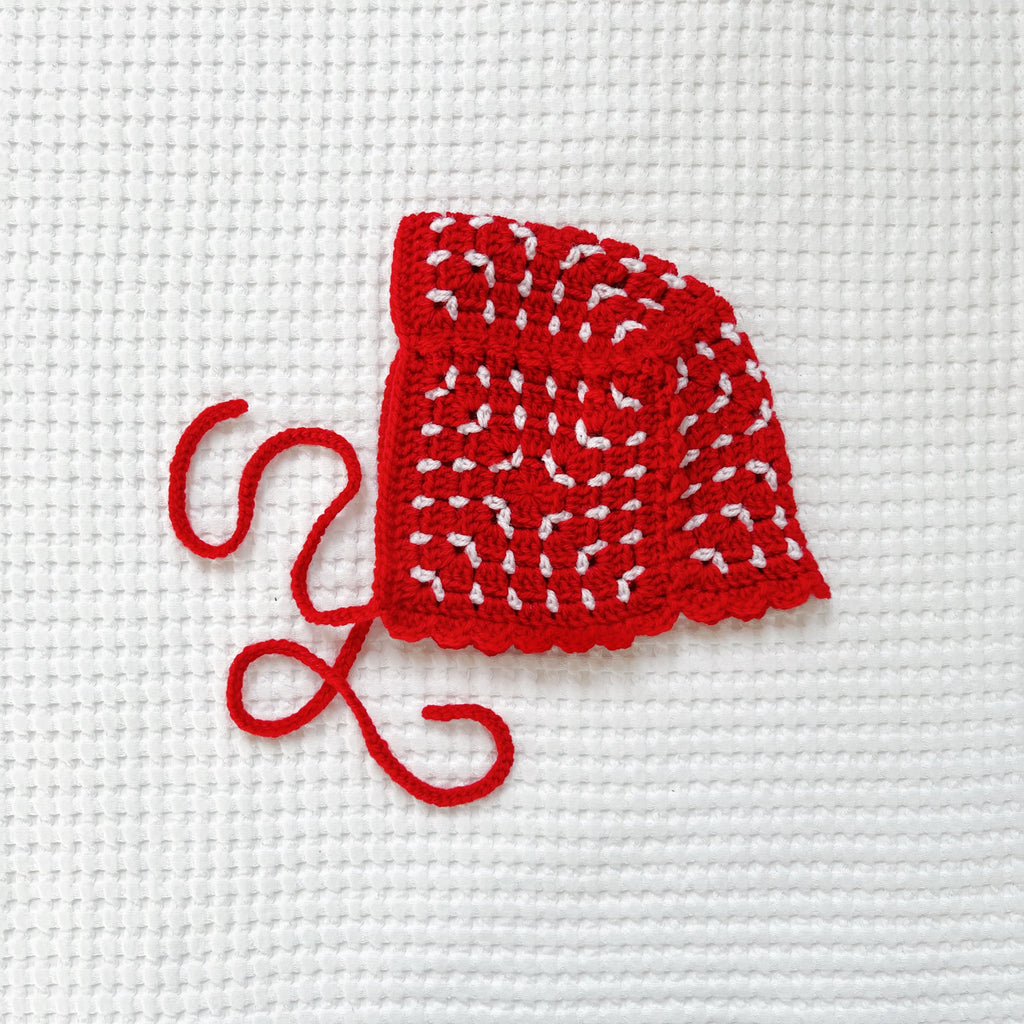 Crocheted red bonnet on a white fabric background