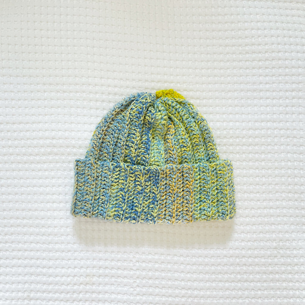 Crocheted beanie with blue and green pattern on a textured white background