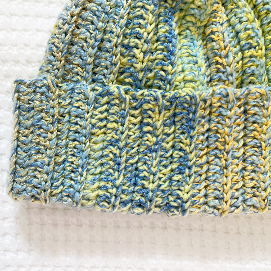 Close-up of a crochet beanie with blue and yellow pattern on a textured white background