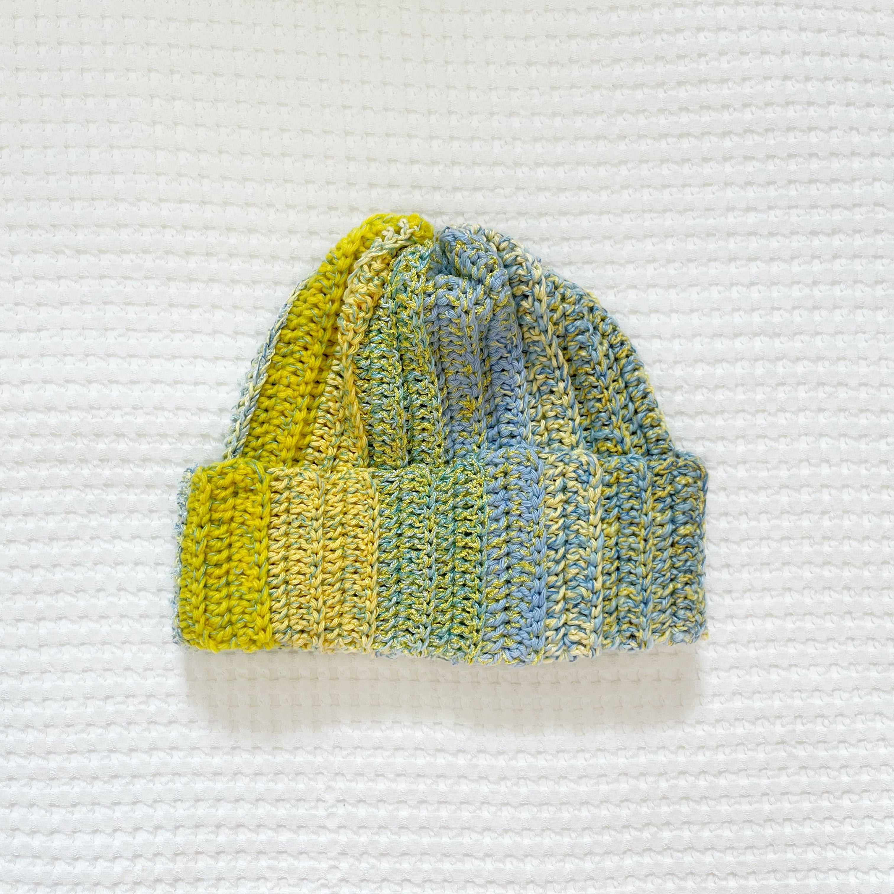 Crocheted beanie with yellow and blue pattern on a textured white background