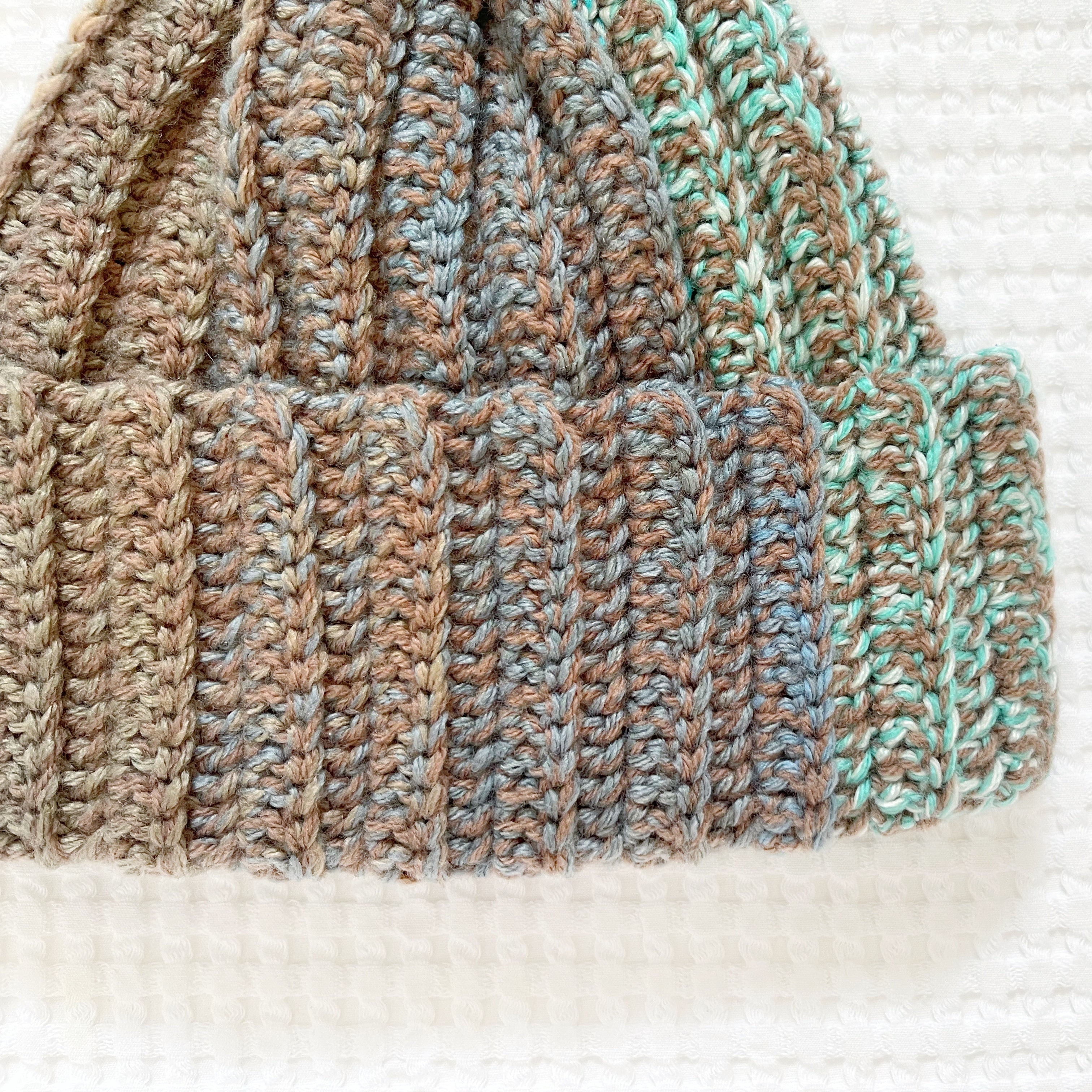 Crochet beanie with ribbed pattern in brown, green, and beige on a textured white background