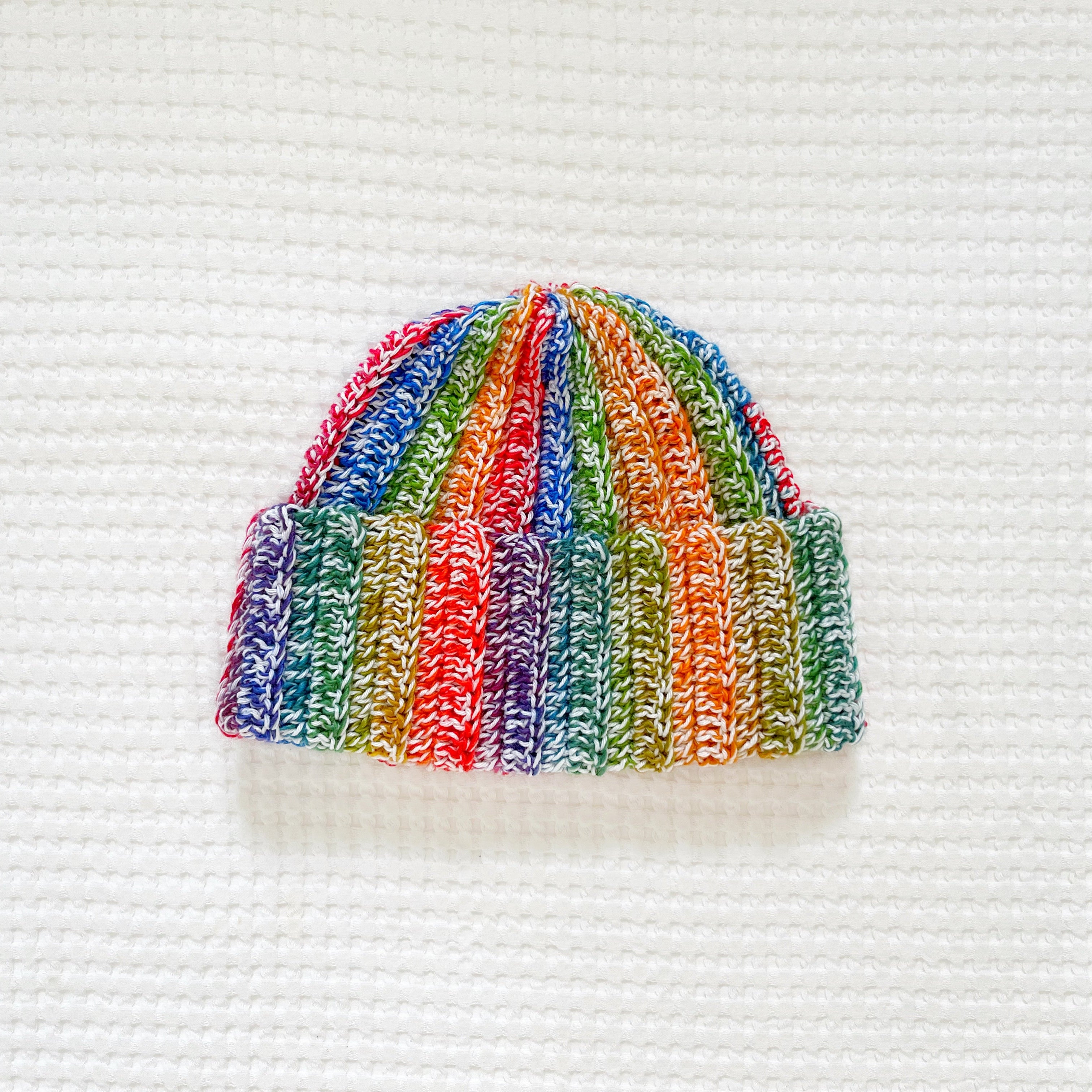 Rainbow colorful striped crochet beanie on a textured white background