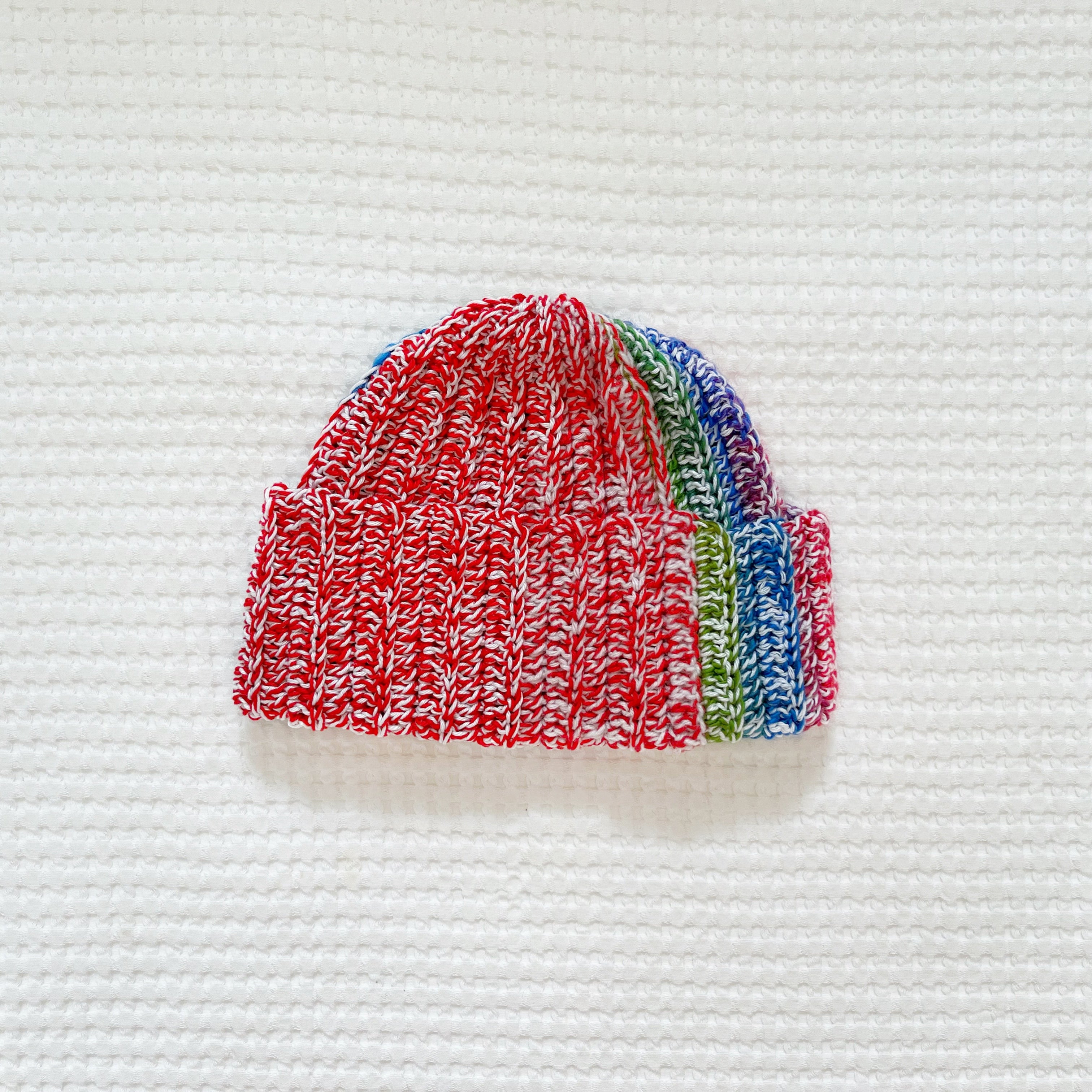 Rainbow colorful crochet beanie on a textured white background